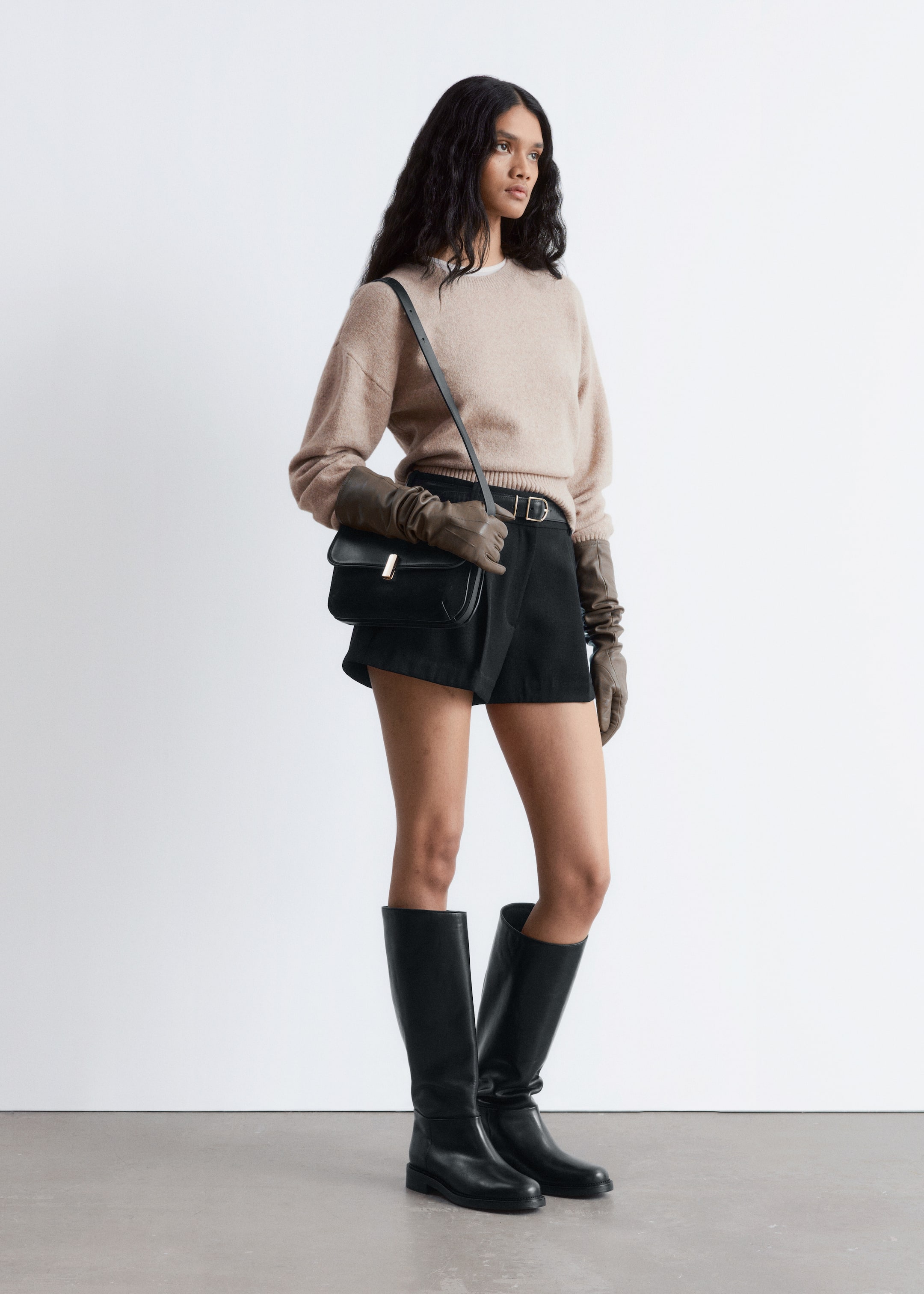 Größeres Bild anzeigen: Schwarze kniehohe Lederstiefel werden aus einem leichten Seitenwinkel präsentiert, wobei ihr gerader, unverzierter Schaft, die abgerundete Spitze und die flache Sohle zur Geltung kommen.