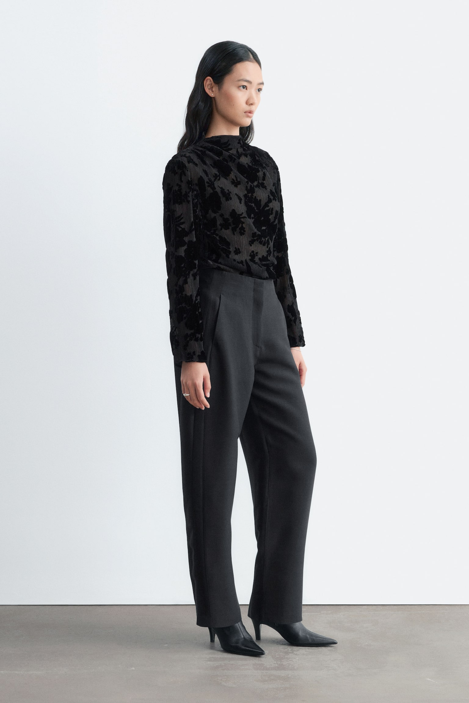 Estos pantalones negros de talle alto estÃ¡n orientados hacia el frente y muestran una silueta estructurada de pernera barrel ligeramente curvada, con detalle de costuras verticales en los laterales. El diseÃ±o presenta una cinturilla limpia y minimalista con cierre frontal oculto y bajos de corte recto ligeramente cropped. - 1