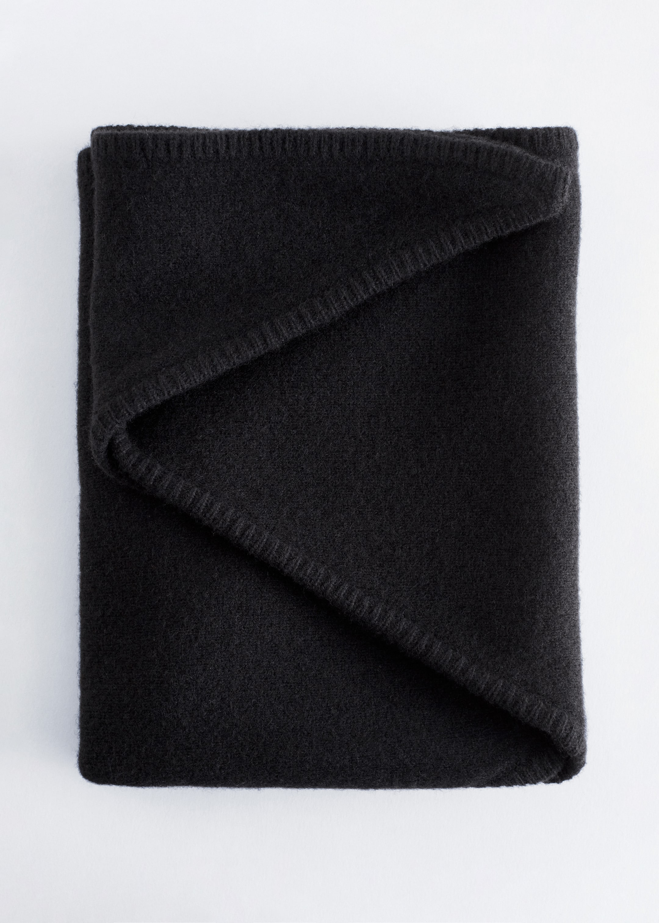 Visualizza immagine più grande: Una sciarpa triangolare nera è piegata con cura, mostrando una texture morbida e uniforme sulla sua superficie e un delicato punto a frusta tono su tono visibile lungo i suoi bordi.