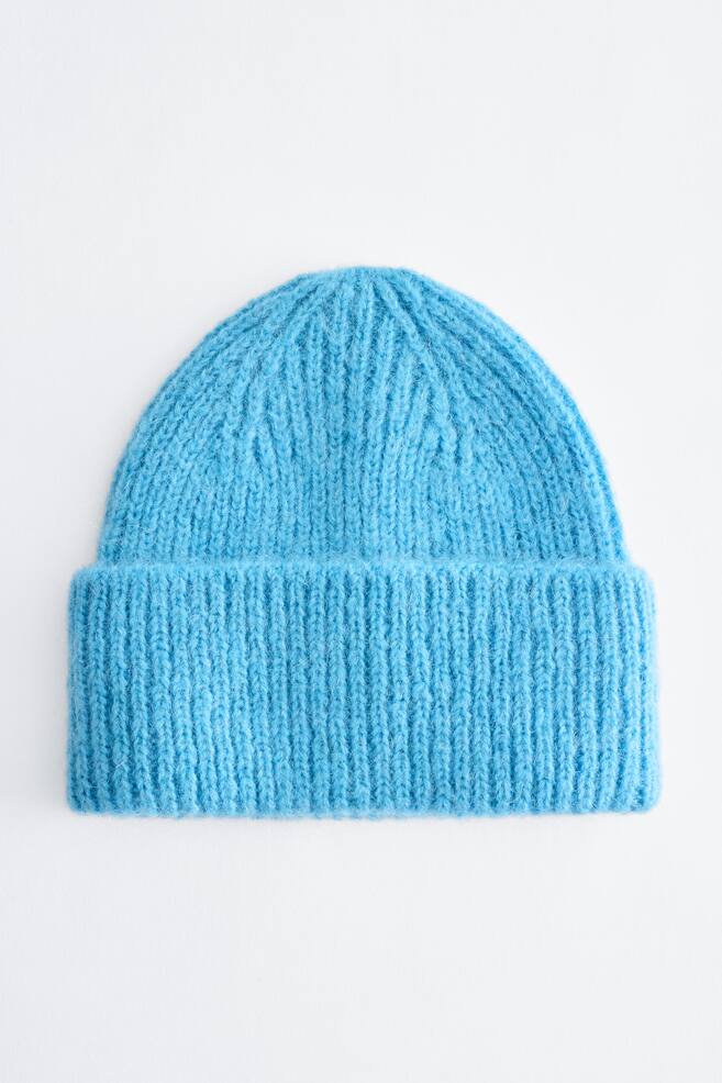Eine hellblaue Beanie-MÃ¼tze in Rippenstrick ist nach vorne ausgerichtet und zeigt eine weiche, flauschige Struktur sowie einen breiten, umgeschlagenen Bund. Die Beanie prÃ¤sentiert ein vertikales Rippenmuster, das sich zum abgerundeten Oberteil hin verjÃ¼ngt. - 1