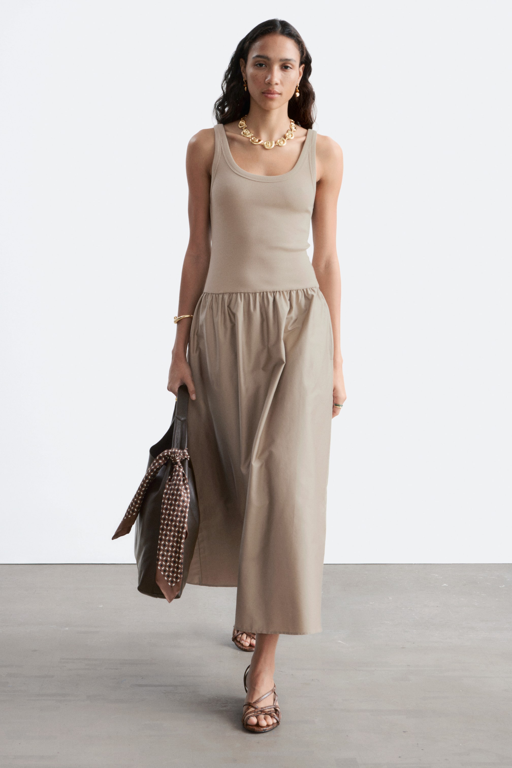 Ver imagen más grande: Un vestido beige que presenta un top ajustado de punto acanalado con cuello redondo, que se transforma en una falda midi fluida y fruncida hecha de un tejido liso, presentado desde una vista frontal.