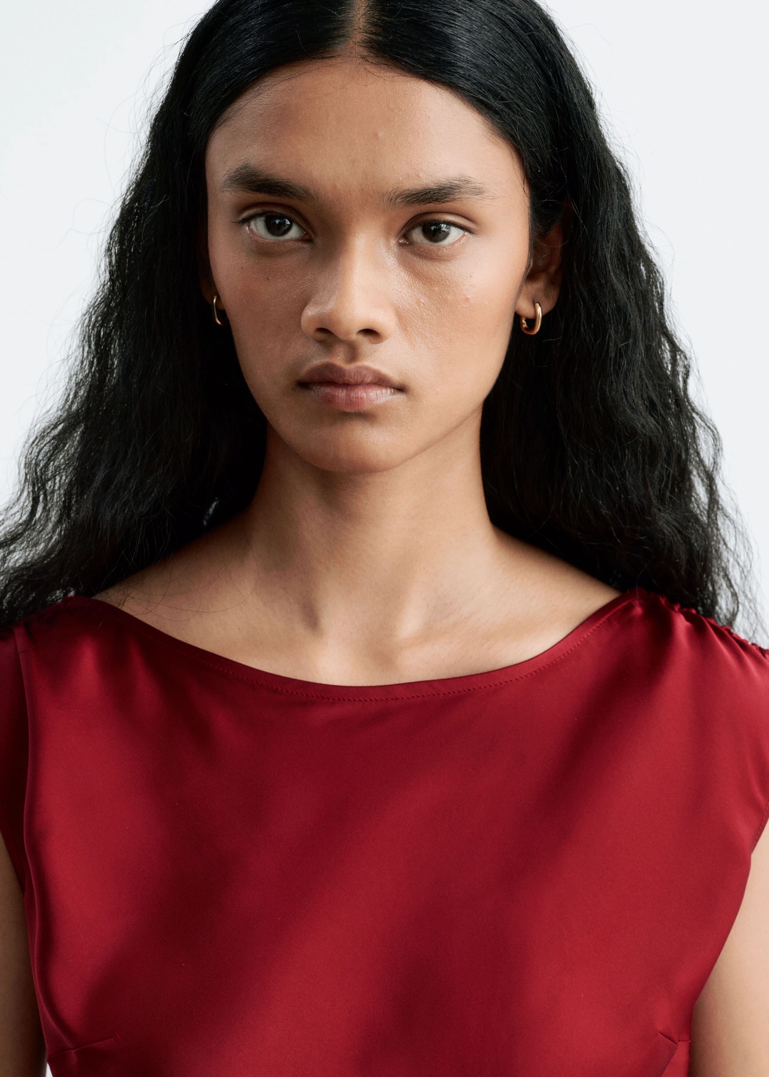 The model is wearing a red satin dress with a wide boat neckline and gathered shoulders. The close-up shot highlights the fabric’s smooth, reflective texture.