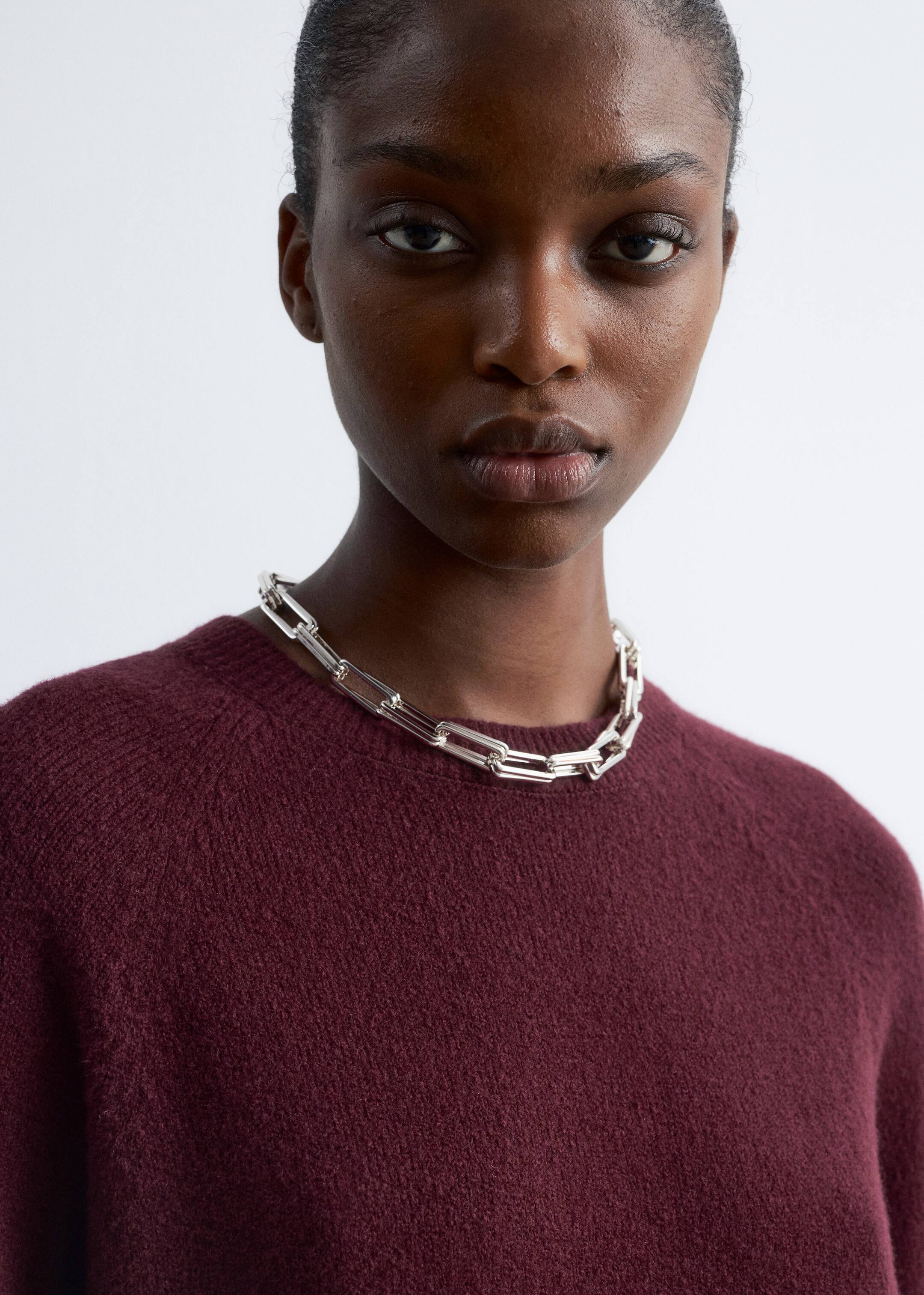 Visualizza immagine più grande: Un maglione bordeaux con scollo a girocollo e maniche raglan viene presentato dalla parte anteriore, indossato. Una collana a catena con maglie spesse in tono argento è appoggiata sullo scollo del maglione.