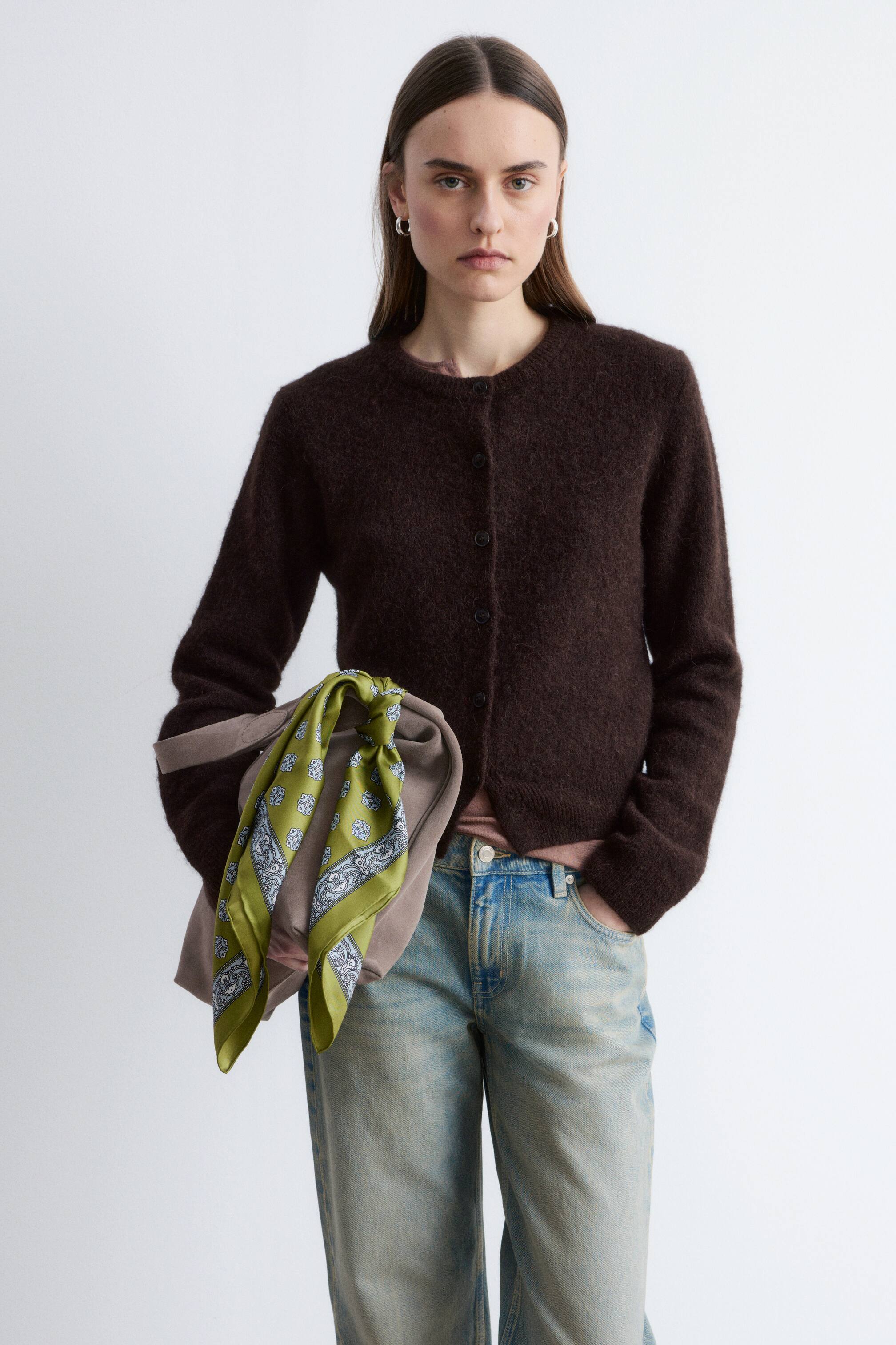 הצגת תמונה גדולה יותר: קרדיגן חום כהה, עם סריגה במרקם, נלבש על ידי הדוגמנית. הוא מעוצב בגזרה ישרה עם גימורים מצולעים וכפתורים בחזית, בשכבה מעל חולצה ורודה בהירה ומשולב עם ג'ינס בגוון שטיפה בהיר.