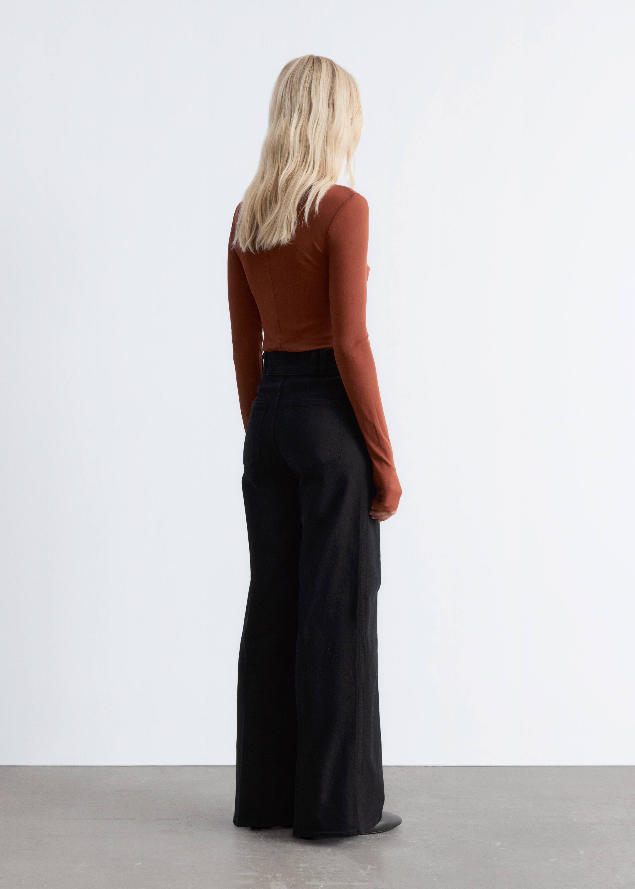 View larger image: A rust-colored long-sleeved top is being worn with black wide-leg pants, both viewed from the back. The fitted top is being tucked into the high-waisted pants, which are featuring visible back pockets and a full-length hem.