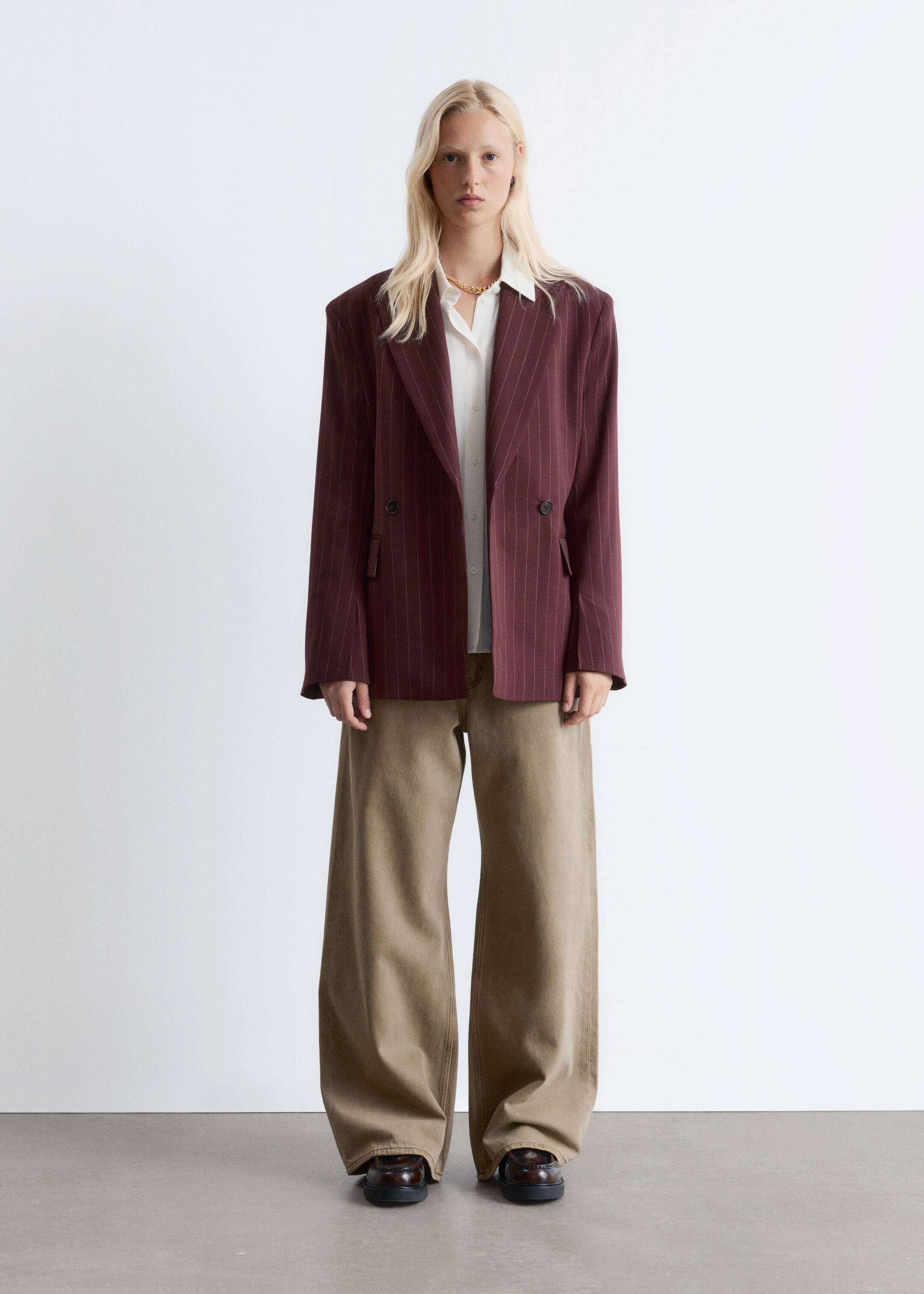 Agrandir l'image: Un blazer croisé à fines rayures rouge foncé avec des revers en pointe, des épaulettes structurées et des poches à rabat à l'avant est porté par le mannequin. Le blazer est porté ouvert sur une chemise blanche.