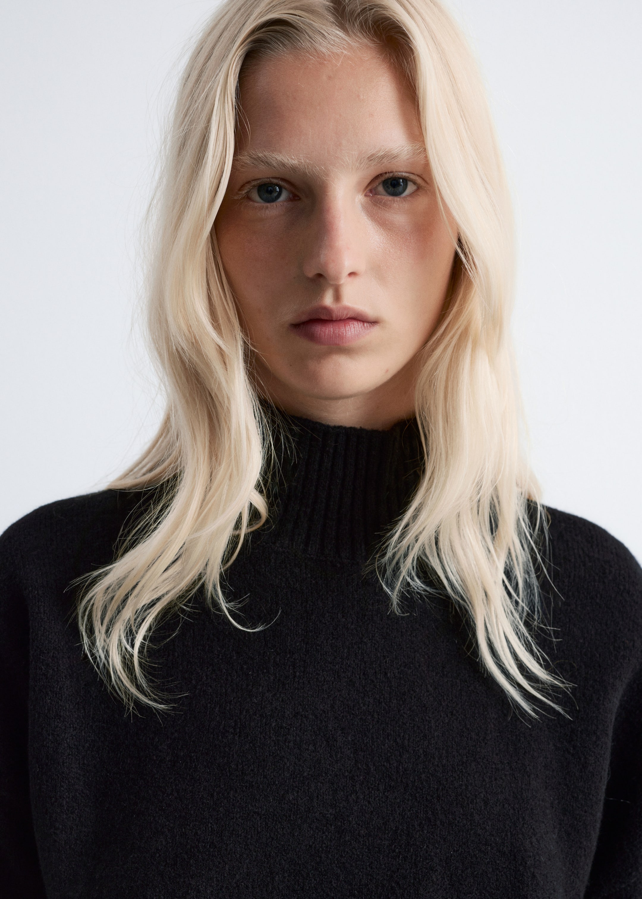 Größeres Bild anzeigen: Ein schwarzer Strickpullover wird präsentiert, der einen Stehkragen und einen weichen, strukturierten Stoff aufweist, der sanft über die Schultern fällt.