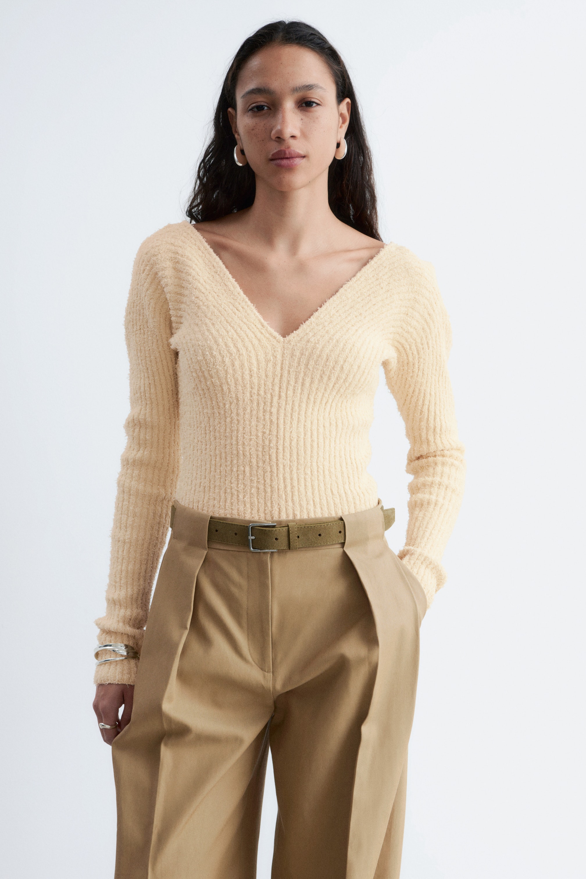 Agrandir l'image: Un haut à col en V en maille côtelée, jaune pâle et duveteux, est présenté, avec des manches longues. Il épouse étroitement les formes du corps.