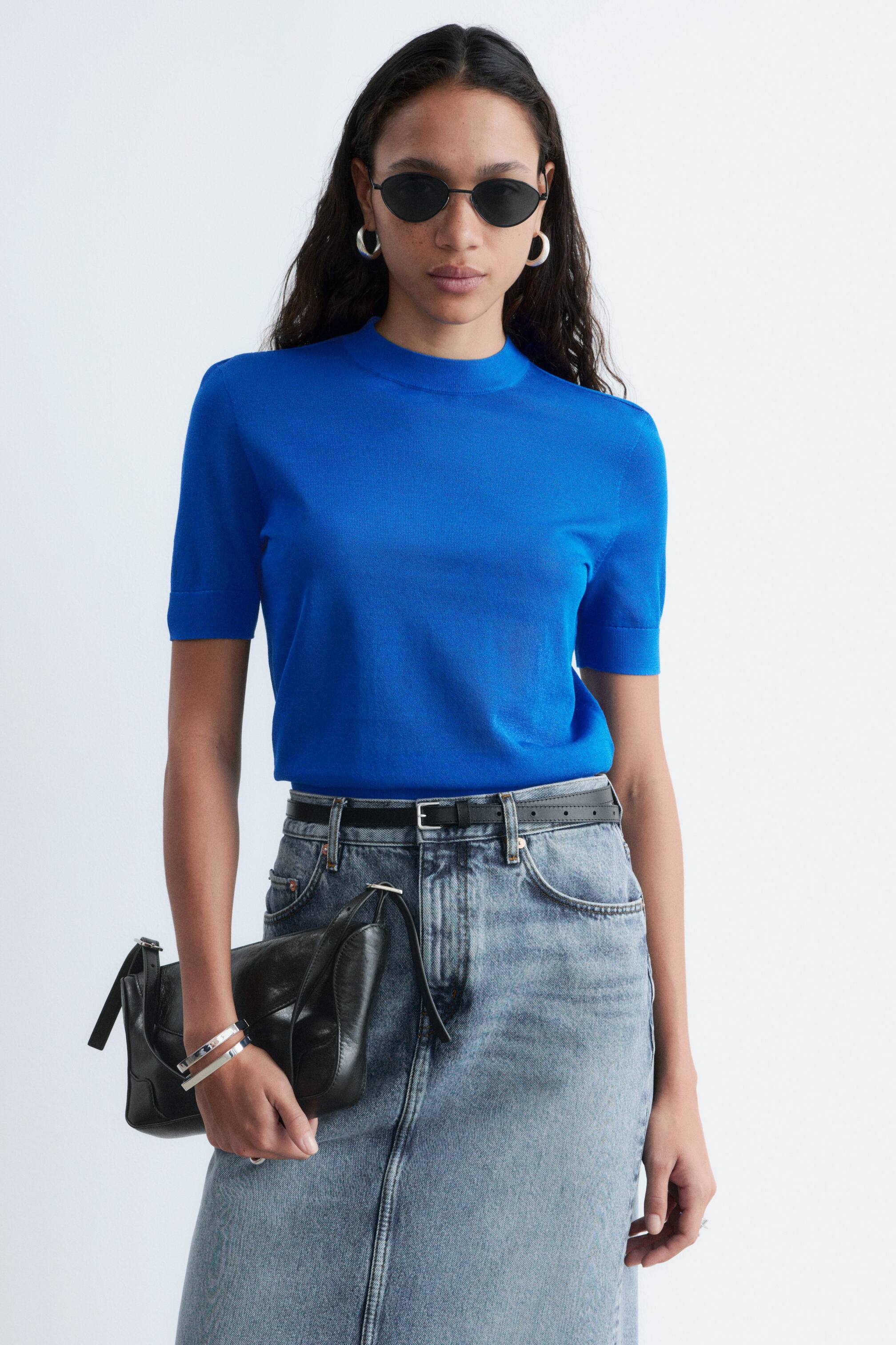 Ver imagem maior: Um top de manga curta em azul royal apresenta uma gola alta simulada e uma textura de malha fina e suave, com a sua silhueta justa a ser mostrada ajustada na cintura.
