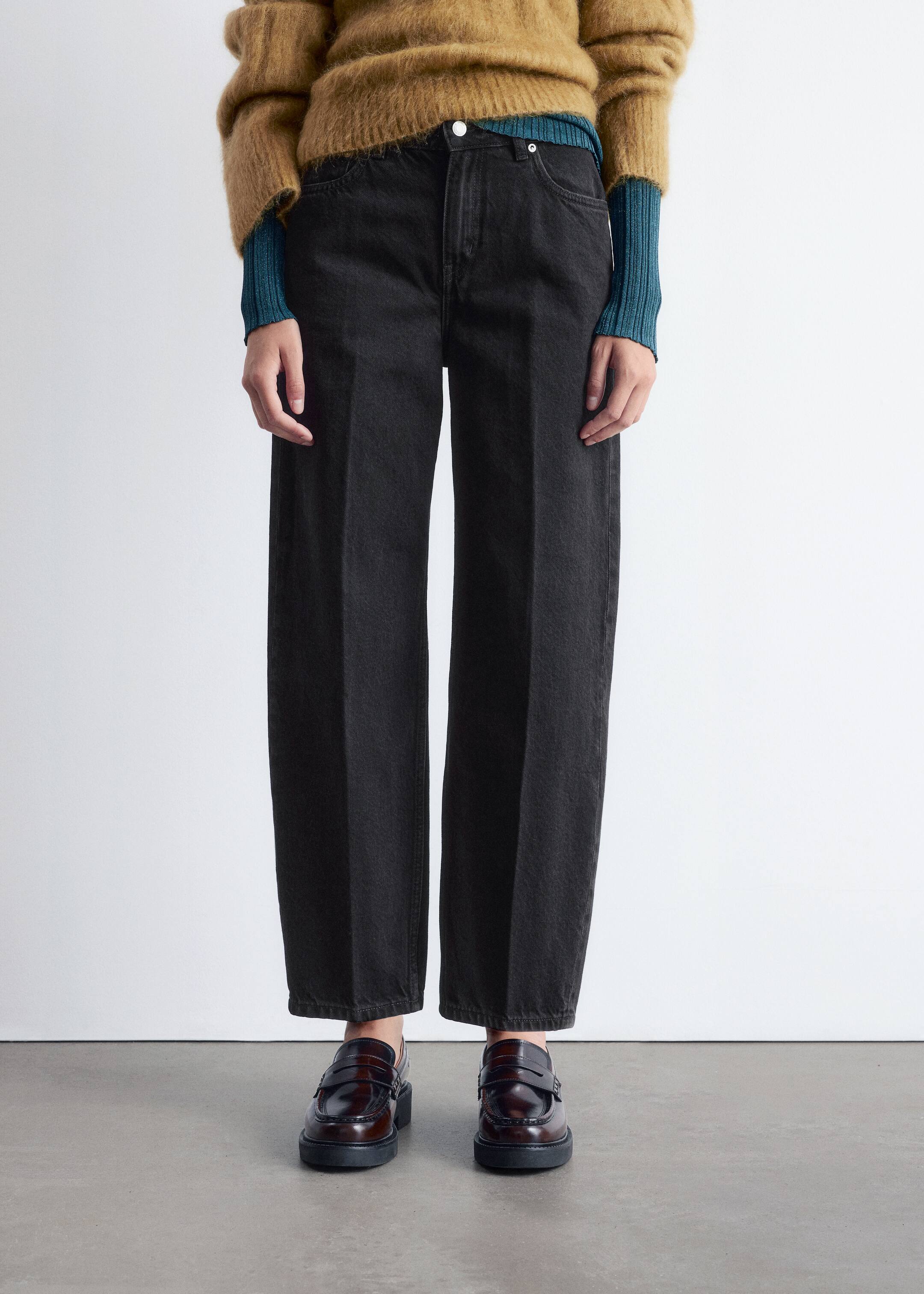 Grösseres Bild ansehen: Gewaschene schwarze Denim-Jeans werden frontseitig präsentiert, mit einer hoch taillierten, entspannten Passform und einem weiten Bein. Sie zeigen einen sichtbaren Knopfverschluss und Fronttaschen, während ihr voller Saum auf dunklen Loafers ruht.
