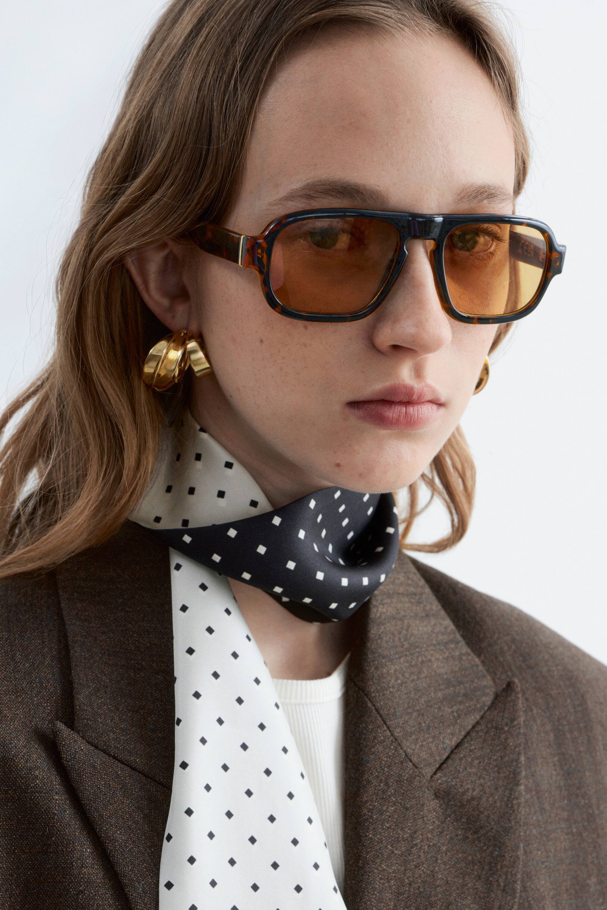 Visualizza immagine più grande: Gli occhiali da sole presentano una montatura tartarugata con aste spesse e un doppio ponte, che sostengono lenti quadrate con una tinta ambrata. Vengono indossati frontalmente sul viso.