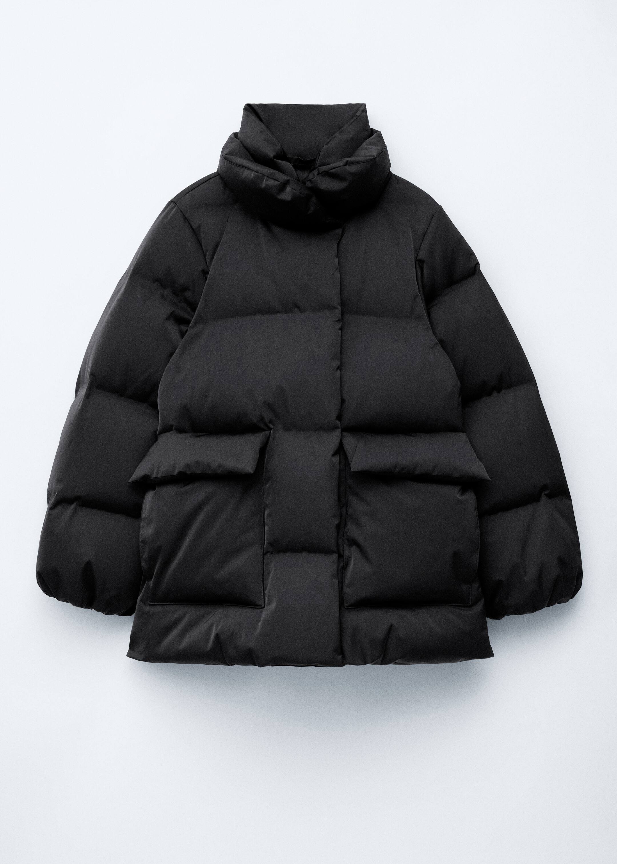 View larger image: A black puffer jacket is laying flat, showcasing its boxy silhouette with heavy padding and distinct quilted sections. It is featuring a high, double stand collar, two large rectangular patch pockets on the front, and a wide placket covering the front closure.