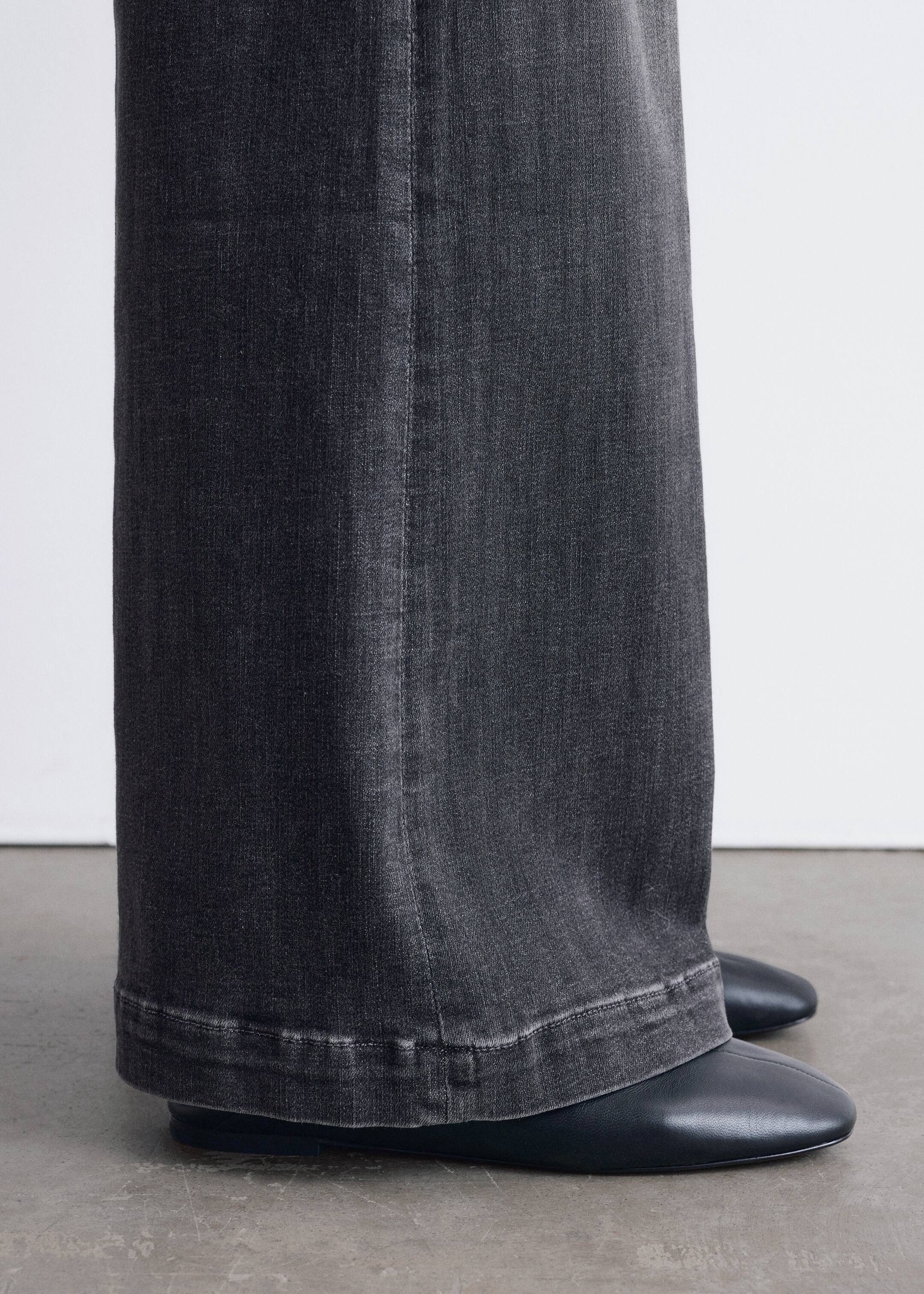 Agrandir l'image: Pantalon en denim gris foncé à jambes larges est présenté d'une vue légèrement de côté. Une couture verticale proéminente descend le long de la jambe, et leur ourlet large et délavé repose sur des chaussures plates noires.