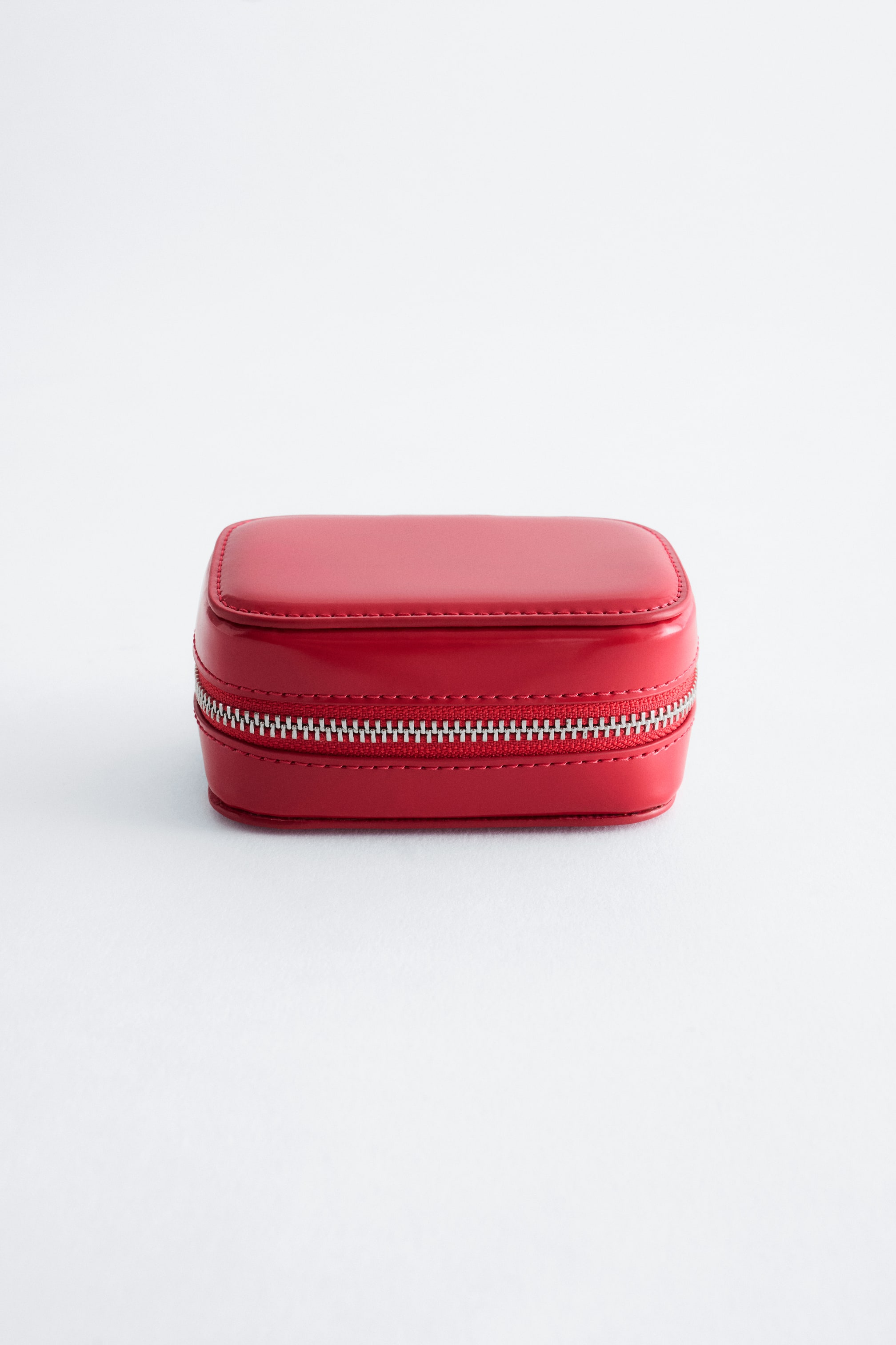 Grotere afbeelding bekijken: Een kleine, rechthoekige rode etui met afgeronde hoeken staat naar voren gericht en heeft een glad, halfglanzend oppervlak met bijpassend rood stikwerk. Een zilverkleurige metalen ritssluiting loopt horizontaal rond het midden van het geheel.