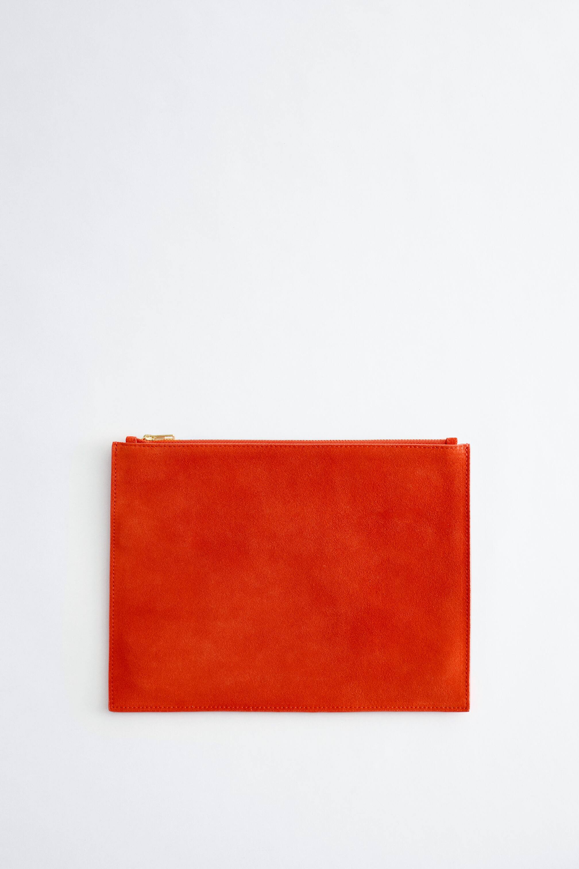 Grösseres Bild ansehen: Ein orangefarbenes, rechteckiges Flachbeutel präsentiert seine Vorderseite, mit einer wildlederähnlichen Textur und sichtbaren Nähten, die seinen Umfang umreißen. Ein goldfarbener Reißverschluss verläuft entlang seiner oberen Kante.