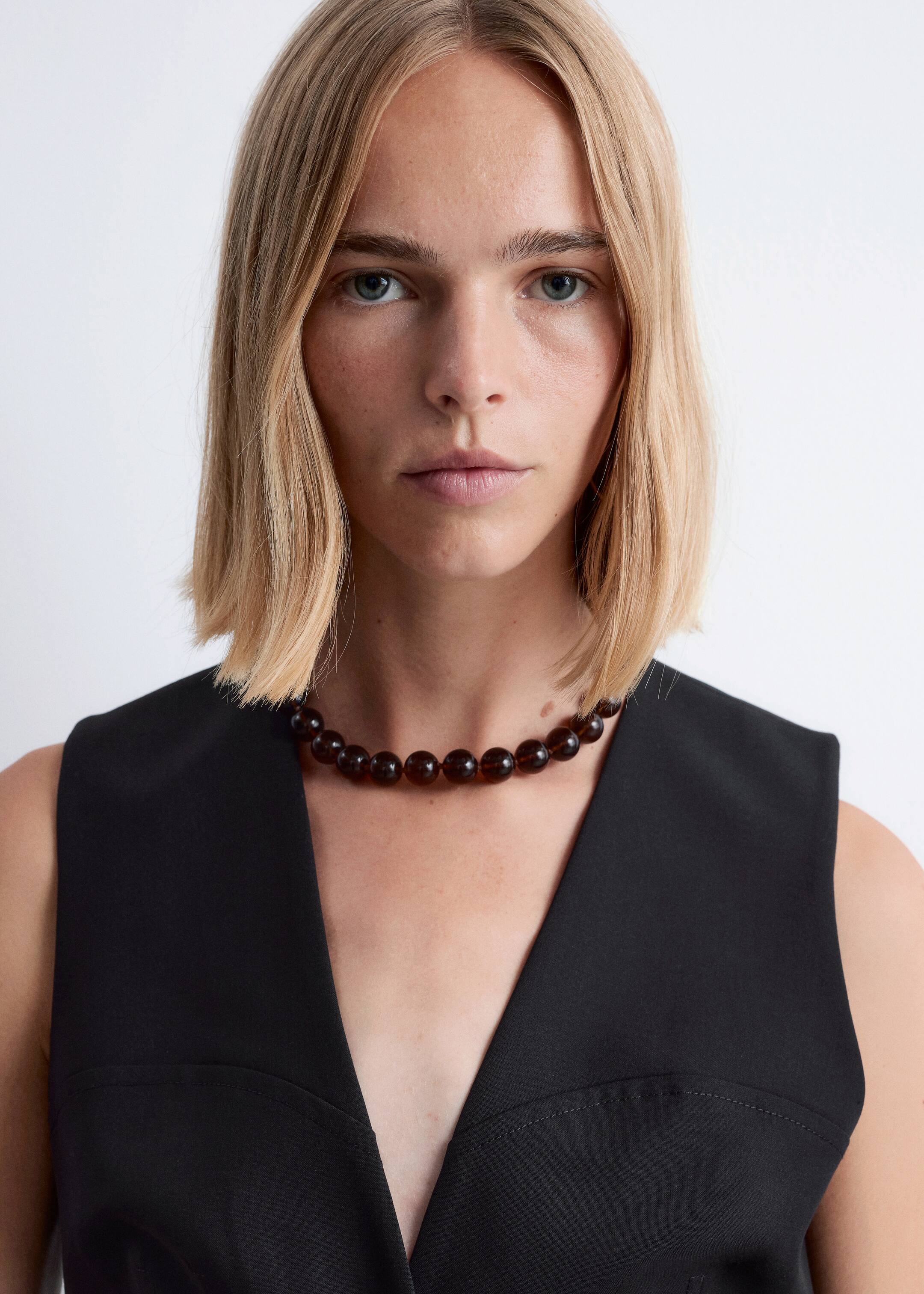 Agrandir l'image: Un collier de perles translucides brun foncé est porté autour du cou d'une personne, reposant juste au-dessus d'un haut noir à col en V. Le collier est composé de perles rondes et uniformes.