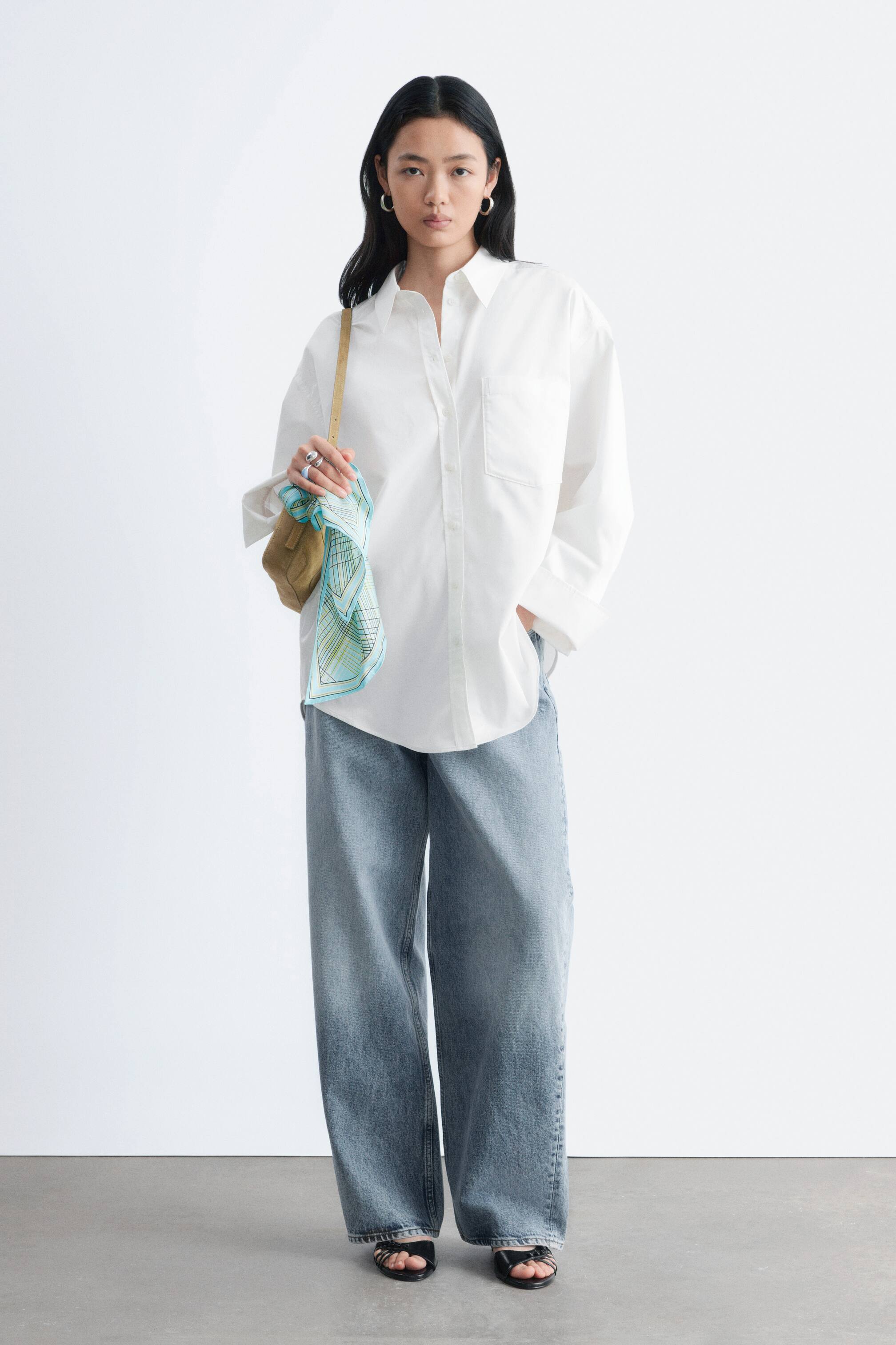 Größeres Bild ansehen: Das weiße Oversize-Hemd zeichnet sich durch einen klassischen Kentkragen, eine Knopfleiste und eine einzelne aufgesetzte Tasche auf der linken Brust aus. Es ist mit langen Ärmeln, Knopfmanschetten und einem abgerundeten Saum gestaltet und bietet eine entspannte und ungesäumte Passform.