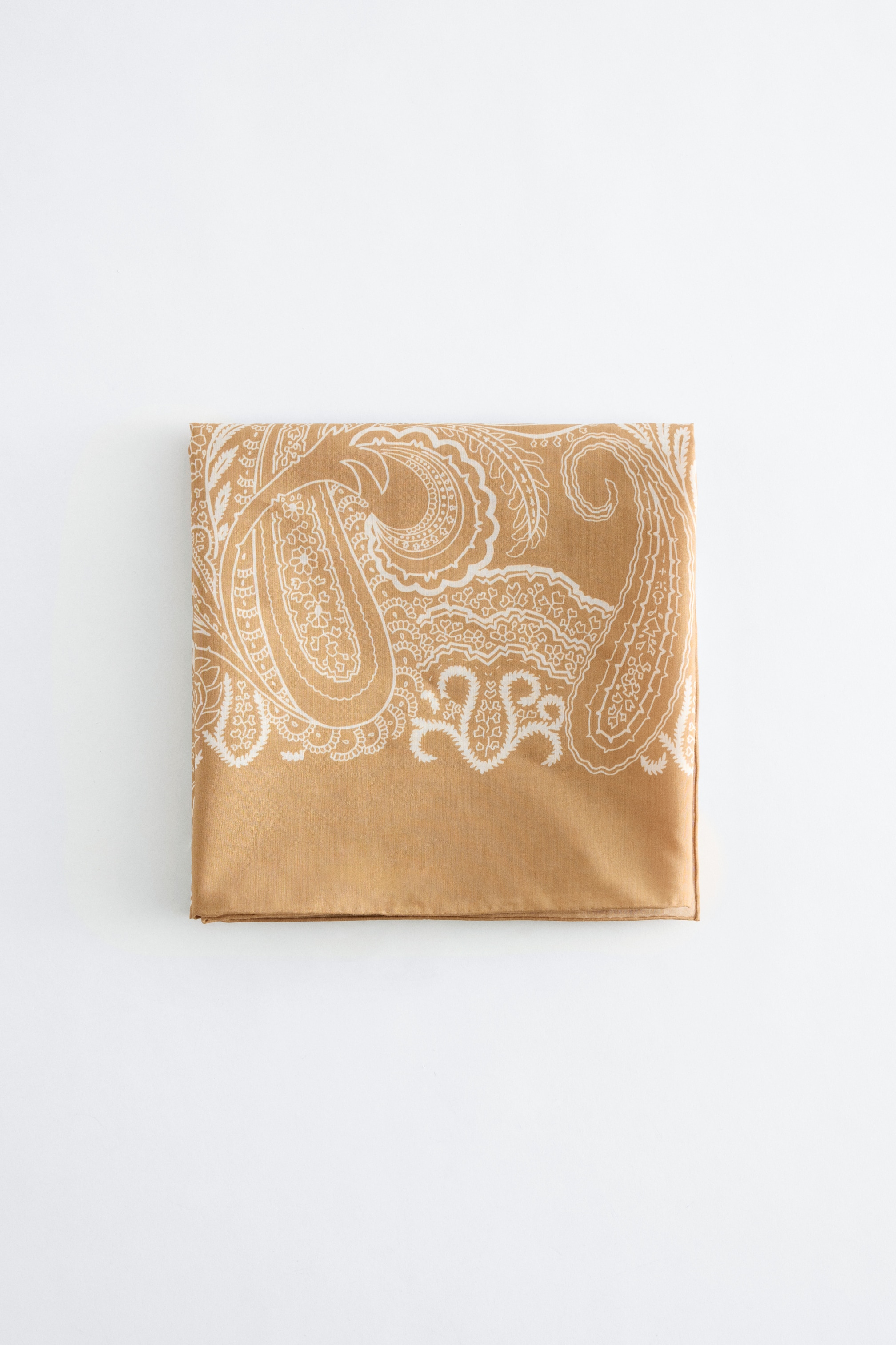 Преглед на по-голямо изображение: "Квадратен шал е сгънат плоско, показвайки светлокафяв цвят с бял пейсли мотив, покриващ горните две трети от видимата му предна повърхност. По долния ръб се вижда плътна светлокафява граница."