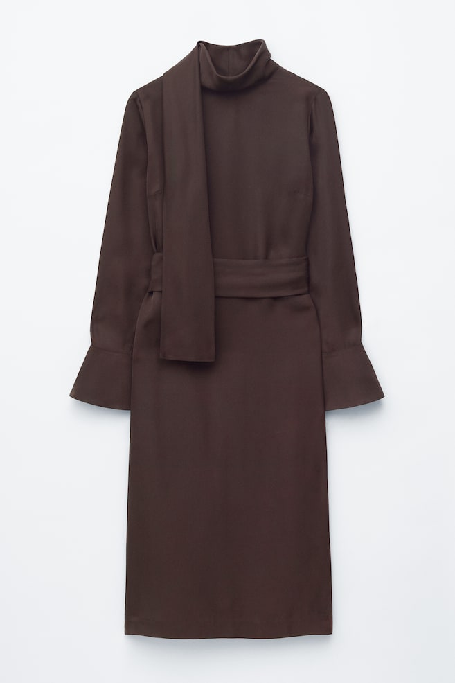 Um vestido midi castanho é apresentado de FRENTE, com uma silhueta reta que se estende até ao meio da perna. Apresenta um decote alto com um lenço drapeado integrado, mangas compridas que terminam em punhos levemente alargados e abotoados, e um cinto do mesmo tecido que ajusta a cintura. - 1