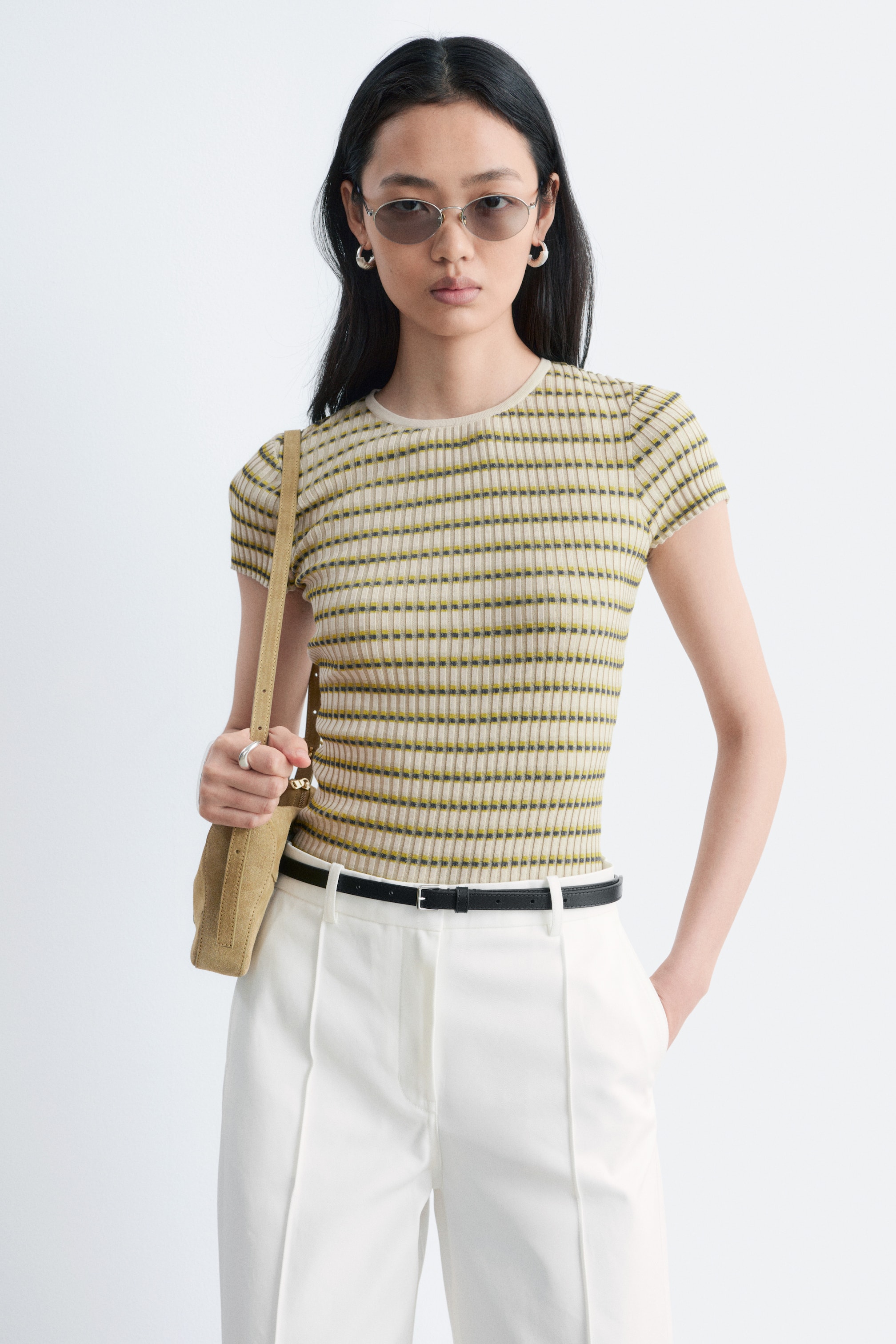 Se større billede: En tætsiddende T-shirt med korte ærmer, der har vandrette grafiske striber og uregelmæssig ribbing i lys beige, olivengrøn og mørkegrå, bæres af modellen. T-shirten er stukket ned i hvide bukser, hvilket fremhæver dens silhuet.