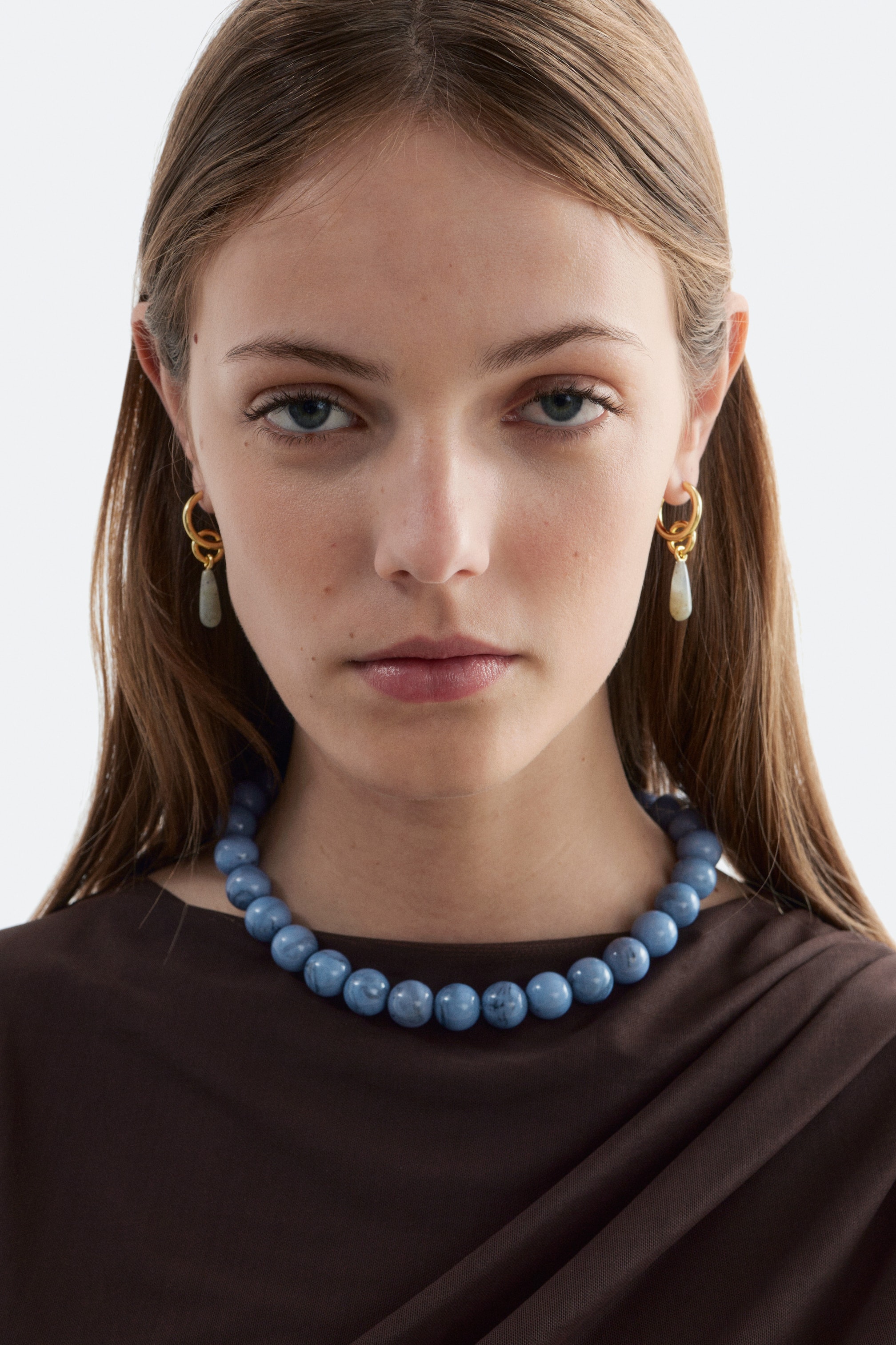 Agrandir l'image: Boucles d'oreilles créoles dorées avec un anneau entrelacé, d'où pend un pendentif en forme de goutte d'eau de couleur claire.