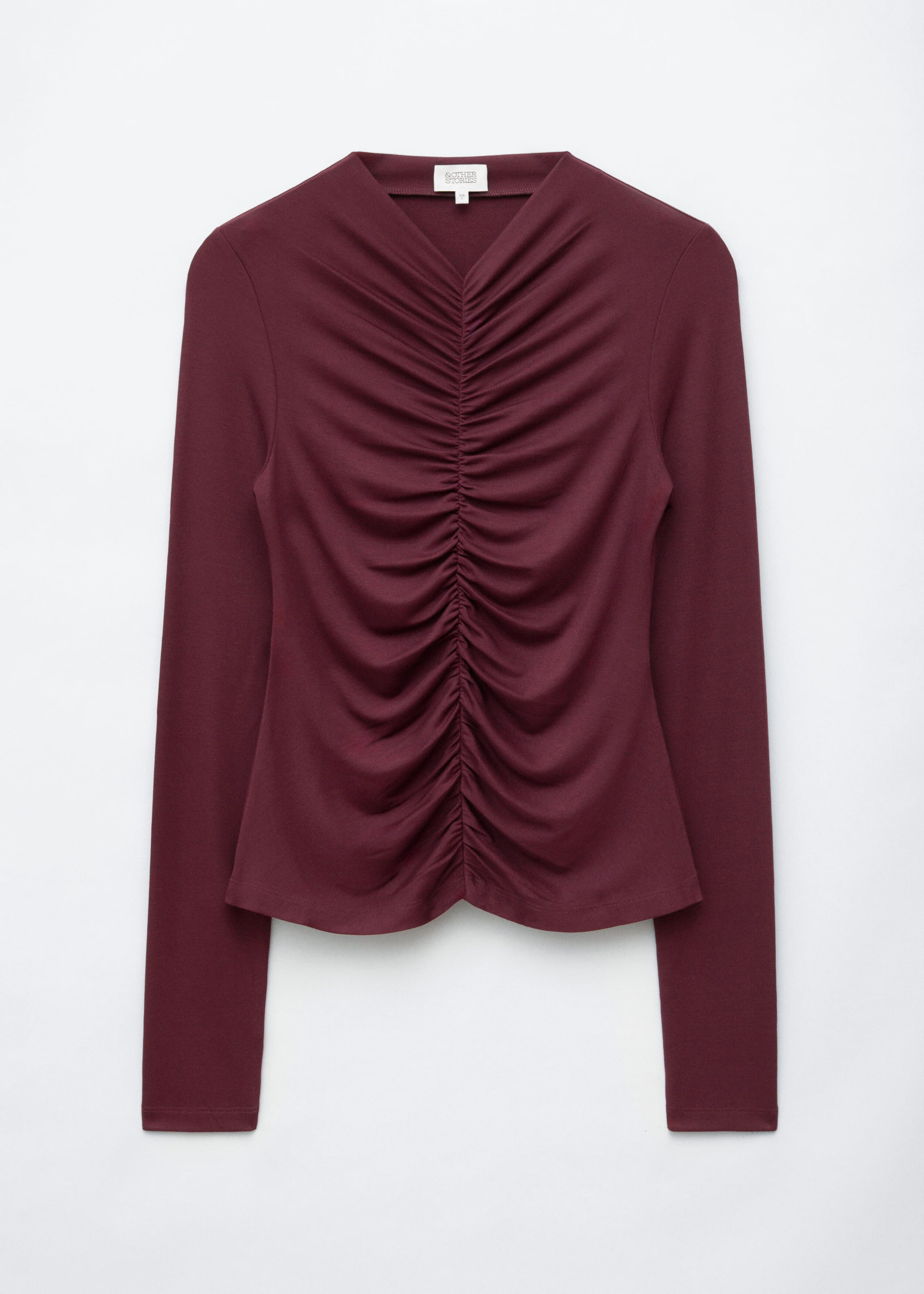A long-sleeved burgundy top is shown from the front, featuring a V-neckline and prominent ruching along the center-front seam that creates gathered draping across the bodice. The top is designed with a fitted silhouette, a slightly curved hem, and long, slim sleeves.