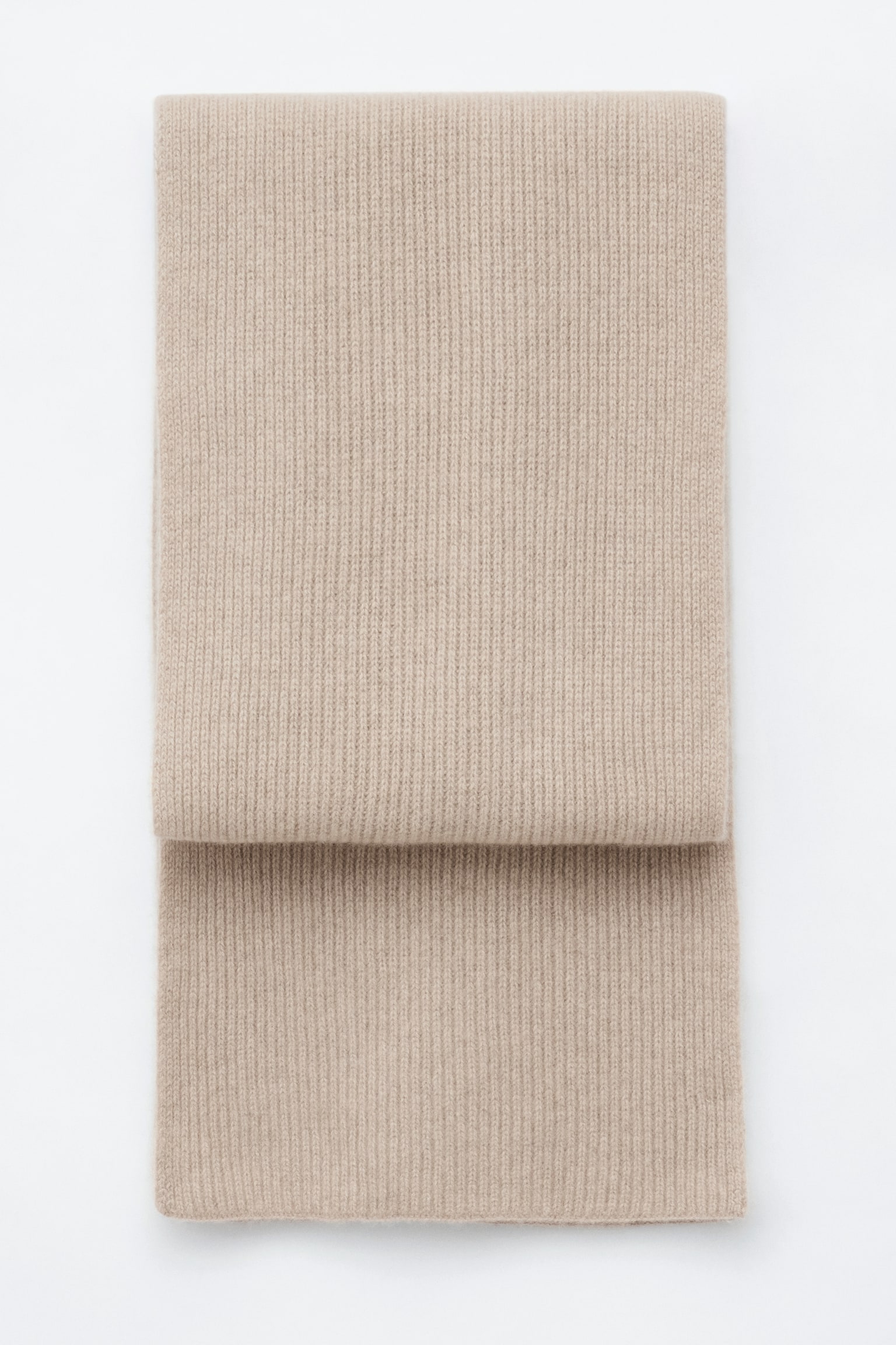 Una sciarpa in maglia di cashmere beige, caratterizzata da una fine texture a coste verticali, Ã¨ adagiata piatta e ripiegata per mostrare la sua struttura a strati dal fronte.