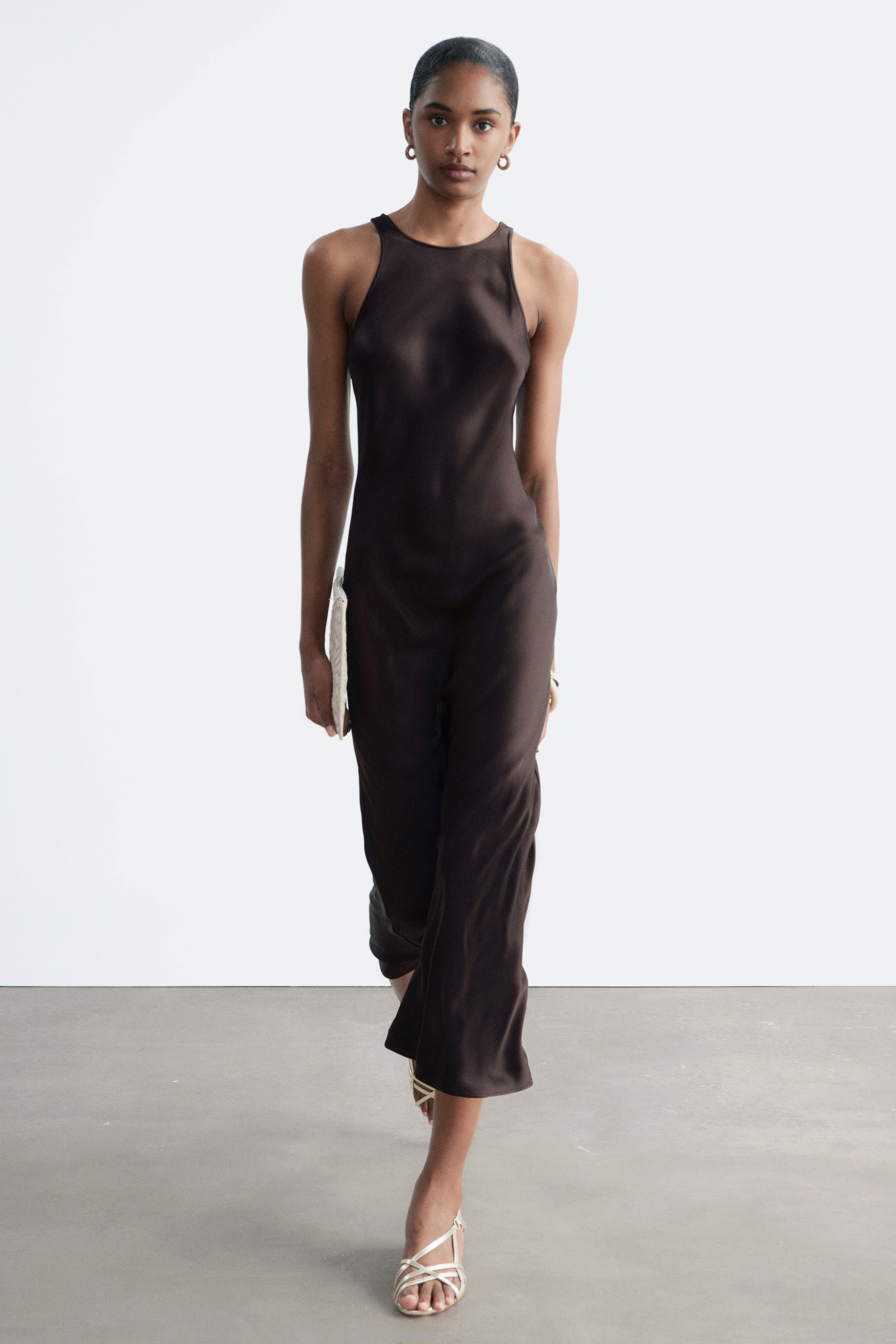 Visa större bild: En mörkbrun satinklänning i midilängd med hög rundad halsringning, breda axelband och en flödande ärmlös silhuett, som visar sin fulla drapering från en framåtvänd perspektiv.