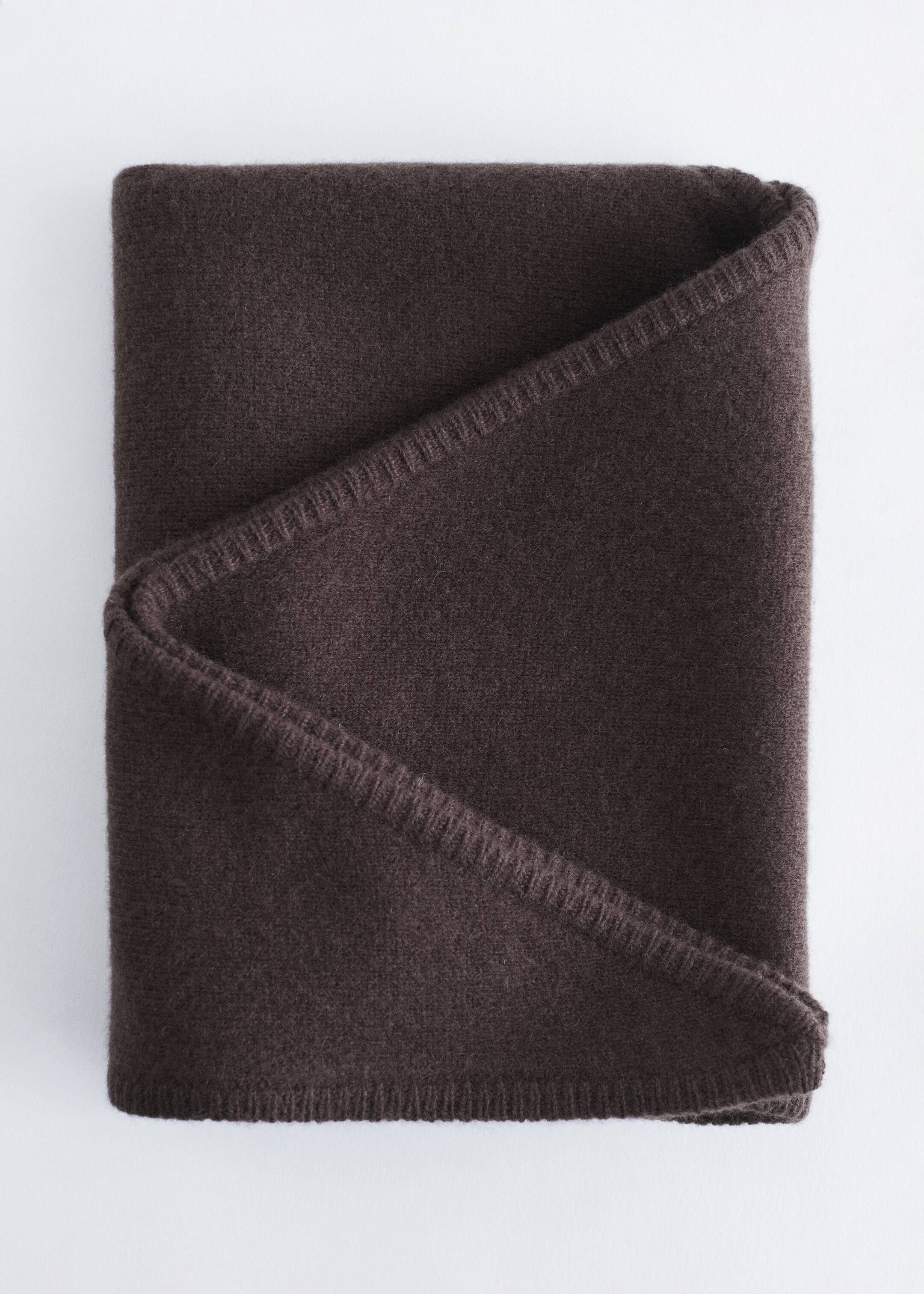 Agrandir l'image: Une écharpe triangulaire en laine brun foncé est pliée en forme rectangulaire, avec un pli diagonal proéminent sur le devant. Ses bords visibles présentent un point de surjet délicat, ton sur ton.