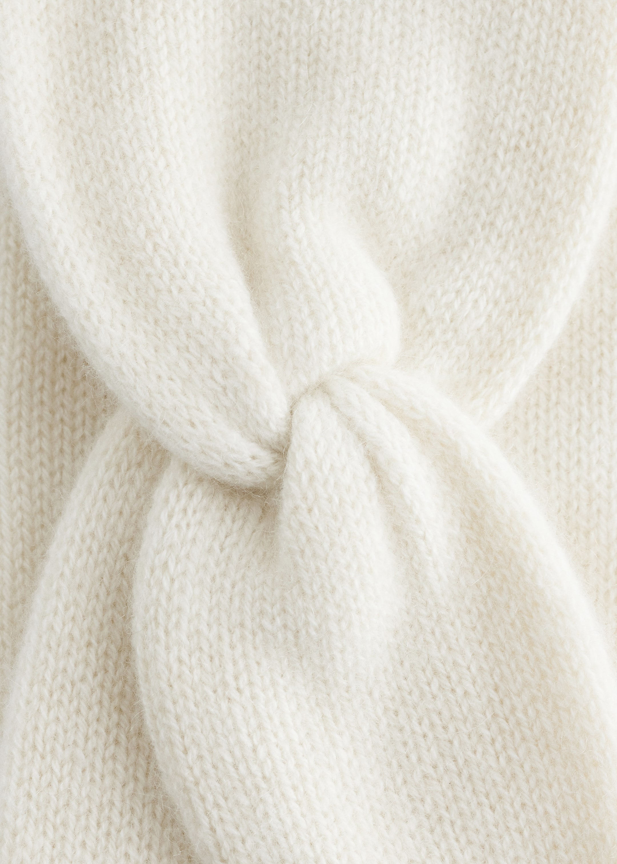 Agrandir l'image: Un bandeau en tricot crème montre son large devant, avec un nœud torsadé central. La texture douce en cachemire est clairement visible.