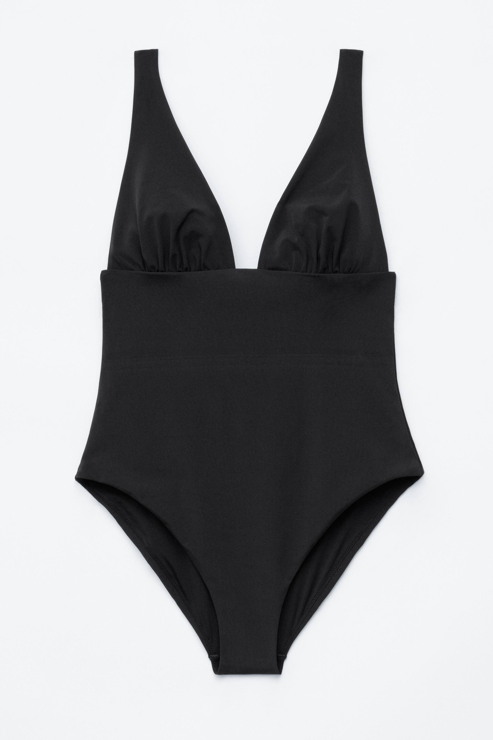 Agrandir l'image: Un maillot de bain une pièce noir est présenté de face. Il se distingue par un profond décolleté en V avec des détails froncés sous la poitrine, une section médiane lisse, et des ouvertures de jambes échancrées.