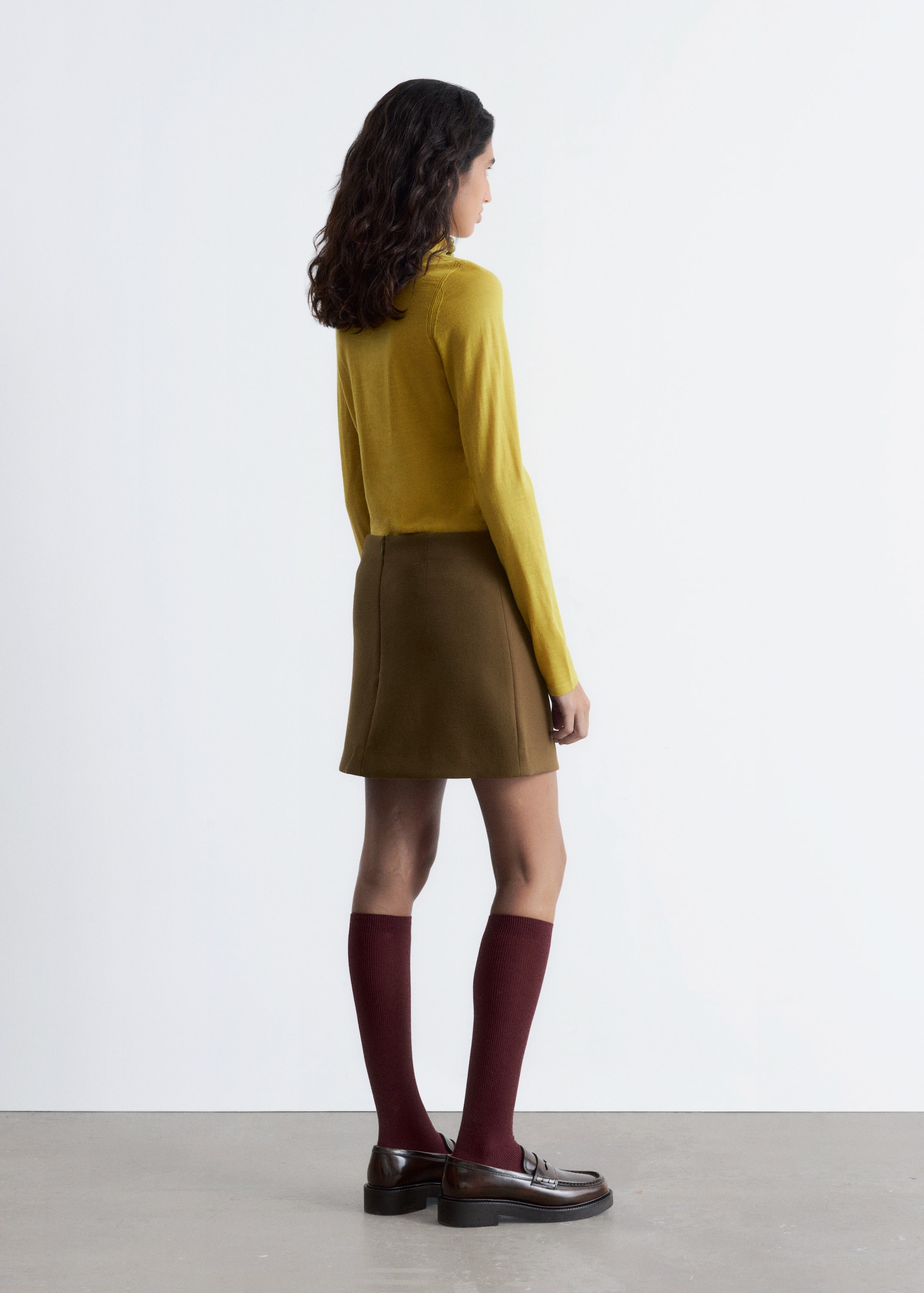 Grösseres Bild ansehen: Ein gelber Rollkragenpullover und ein brauner Minirock werden von der Seite und von hinten gezeigt. Der Pullover hat einen hohen Rollkragen und lange Ärmel, während der Minirock eine A-Linien-Silhouette und einen sichtbaren Reißverschluss auf der Rückseite aufweist.
