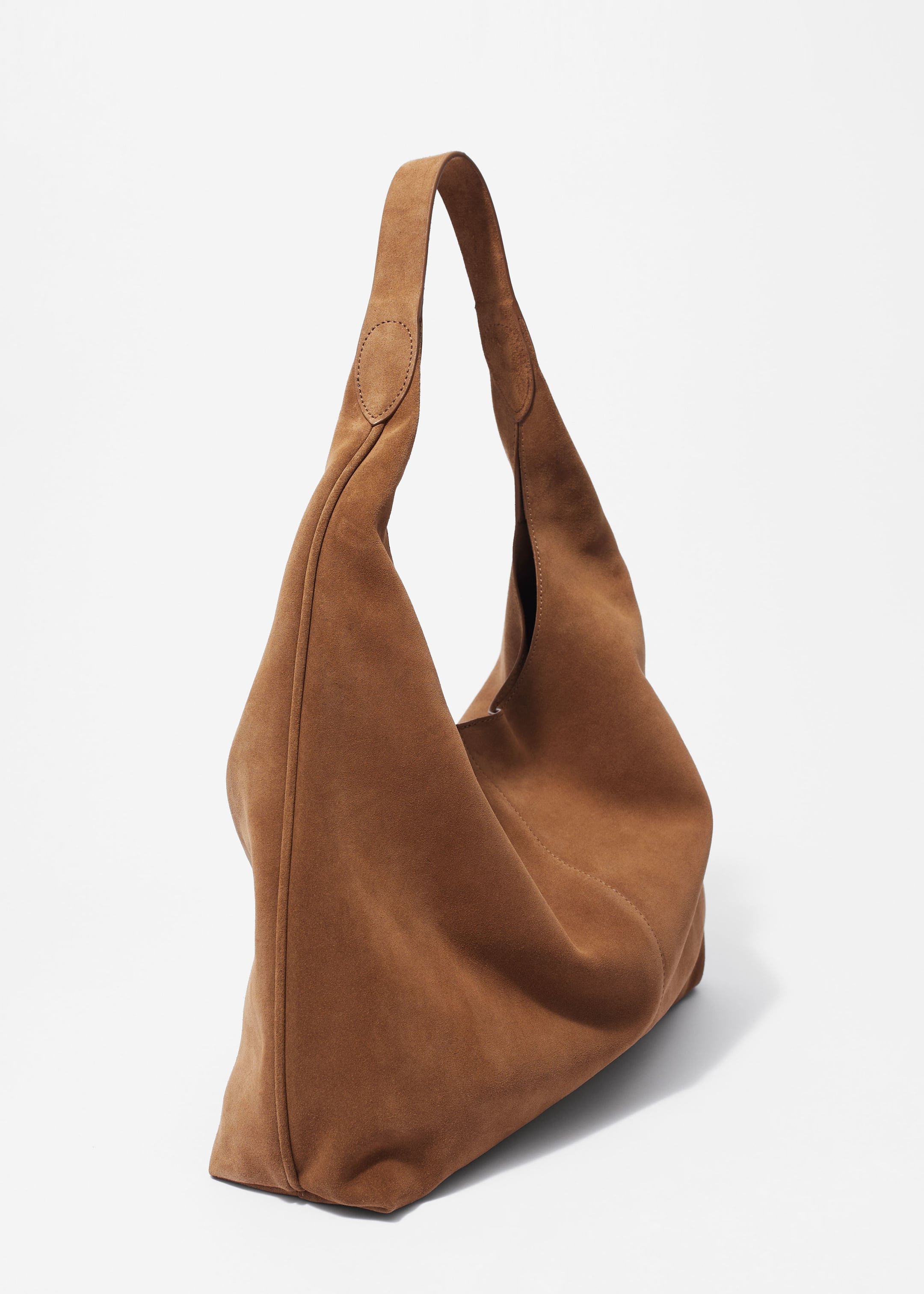 Größeres Bild ansehen: Eine braune Wildleder-Shopper-Tasche steht mit einer glatten, matten Oberfläche und einer markanten vertikalen Naht auf ihrem Körper. Ein einzelner Griff biegt sich nach oben, befestigt mit kreisförmigen Wildlederflecken.
