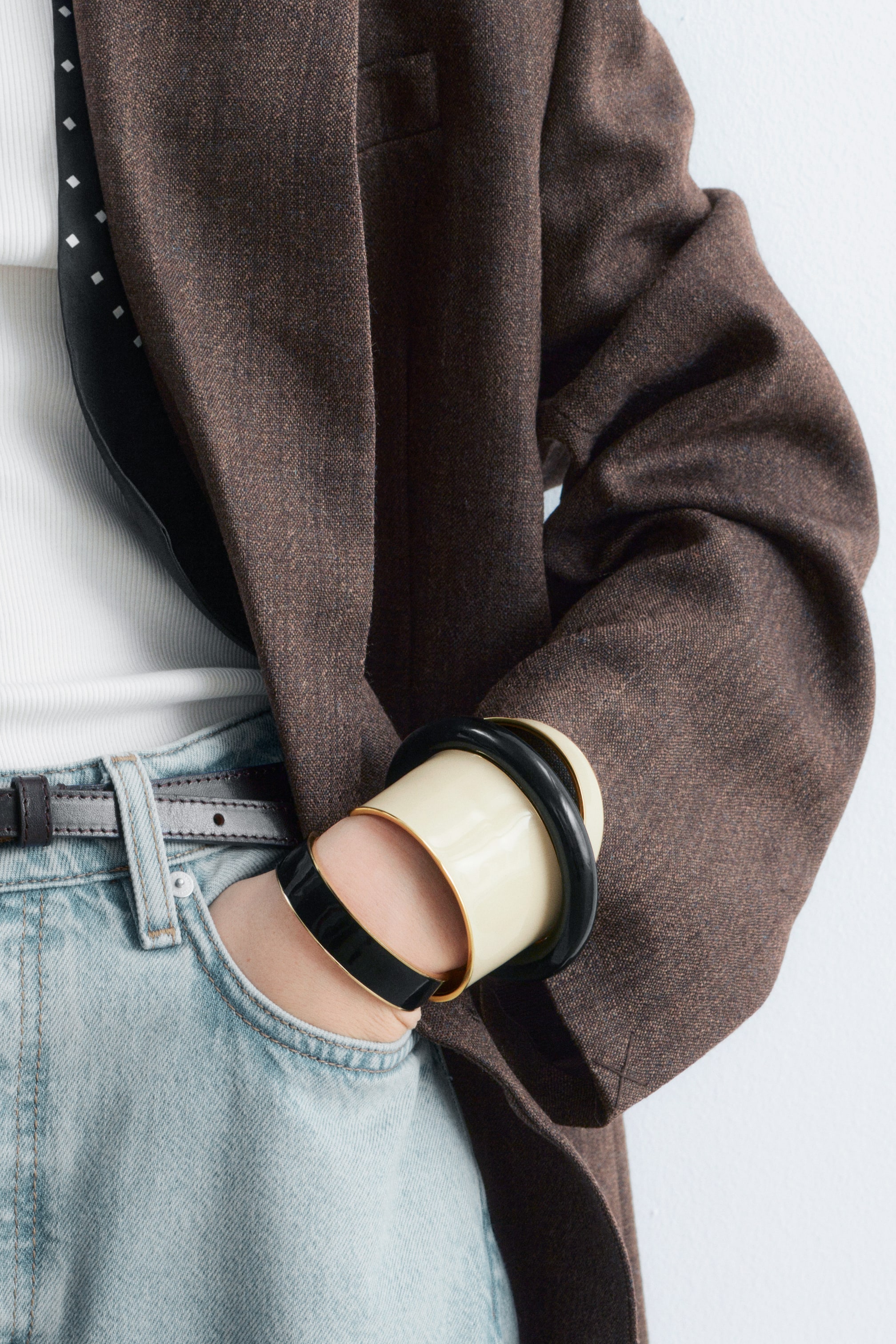 Grotere afbeelding bekijken: Een bruine, gestructureerde blazer wordt gedragen, waarbij de lange mouw is opgestroopt en verschillende zwarte en crèmekleurige armbanden aan de pols zichtbaar zijn.