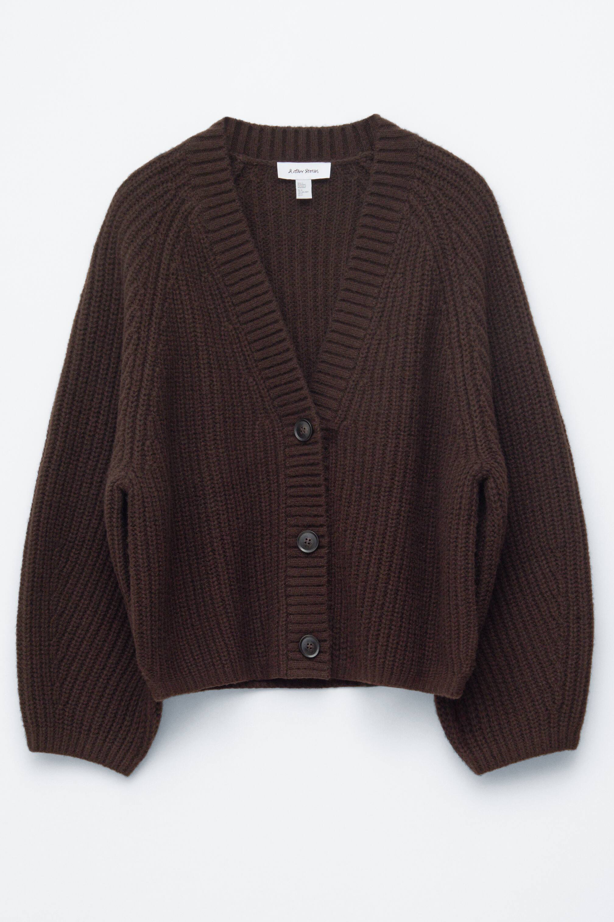 Agrandir l'image: Un cardigan brun foncé est présenté de face, mettant en valeur une texture en maille côtelée épaisse sur toute sa silhouette en forme de cocon. Il est conçu avec un col en V, des manches raglan longues avec des poignets côtelés, un ourlet côtelé et se ferme avec trois grands boutons sombres à l'avant.