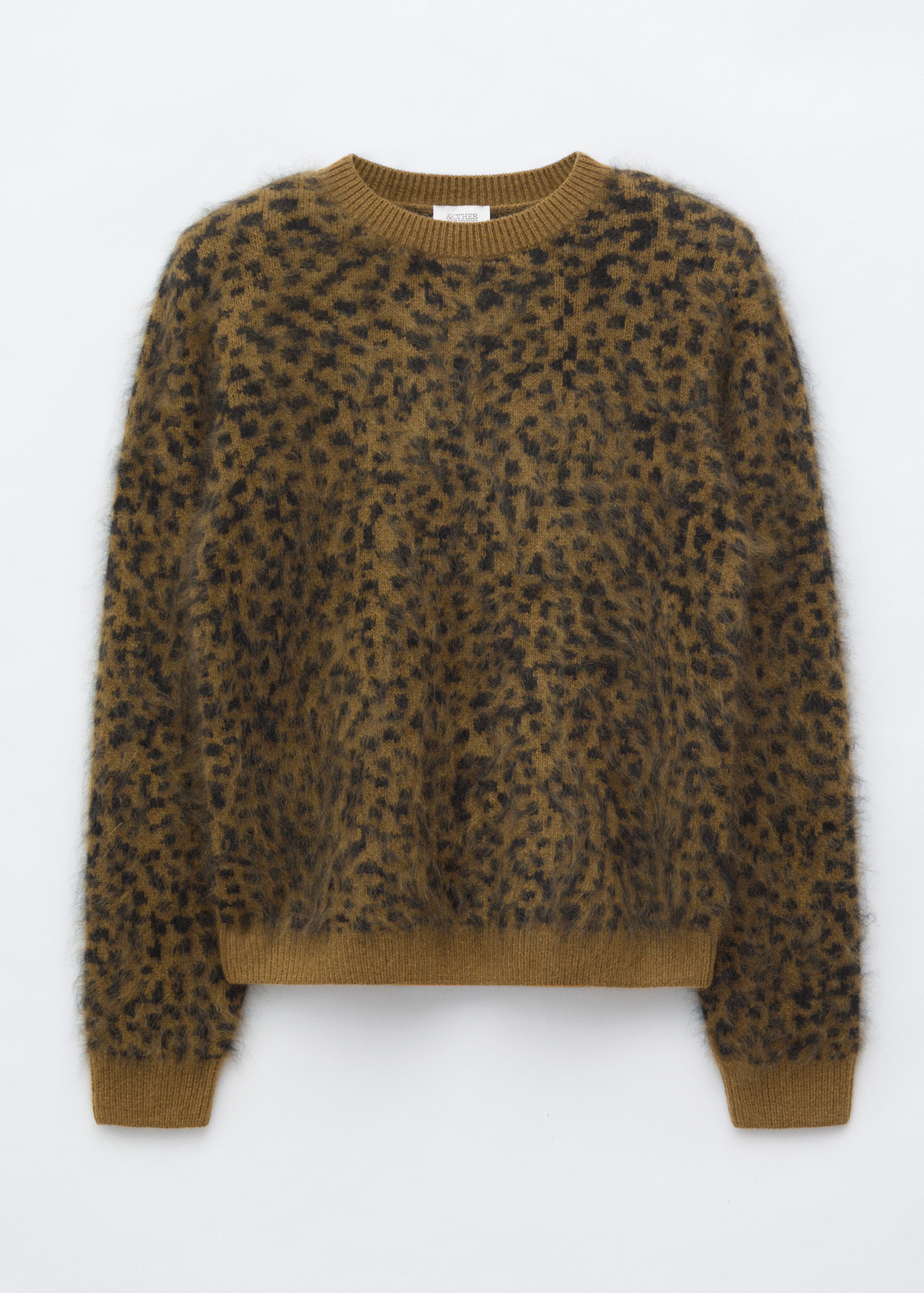 Un pulover din lÃ¢nÄ merinos, cu un tricot pufos, texturat Èi imprimeu leopard maro Èi negru, este purtat de model. Puloverul cu decolteu rotund este stilizat cu pantaloni negri Èi o geantÄ de umÄr din piele Ã®ntoarsÄ maro, purtatÄ pe umÄr.