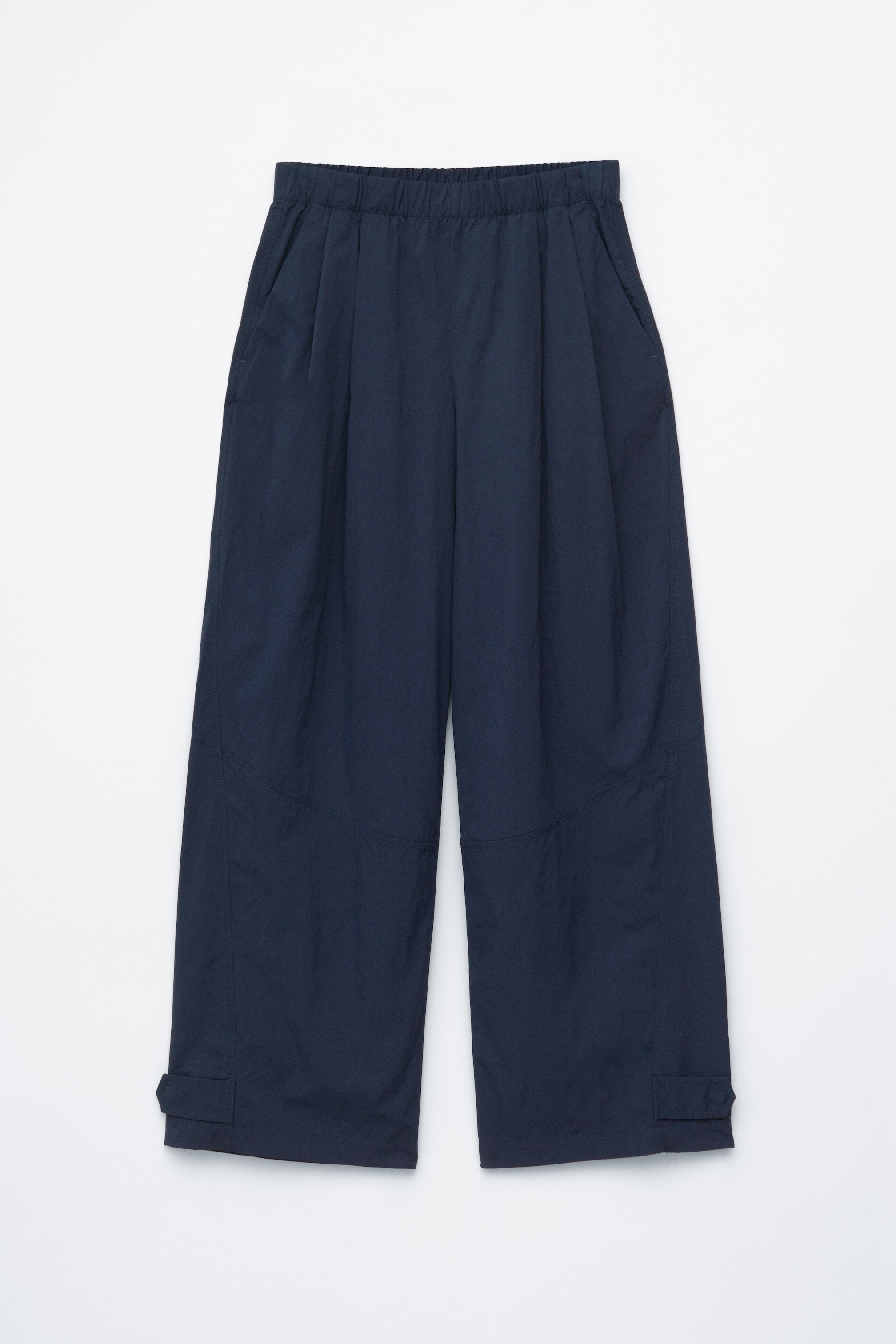 Grotere afbeelding bekijken: Deze marineblauwe broek, gepresenteerd van de VOORKANT, heeft een elastische tailleband, zijzakken en volumineuze barrelpijpen. Ze zijn gedetailleerd met scherpe voorplooien, gebogen snijlijnnaden op de benen en drukknoopjes aan elke zoom.
