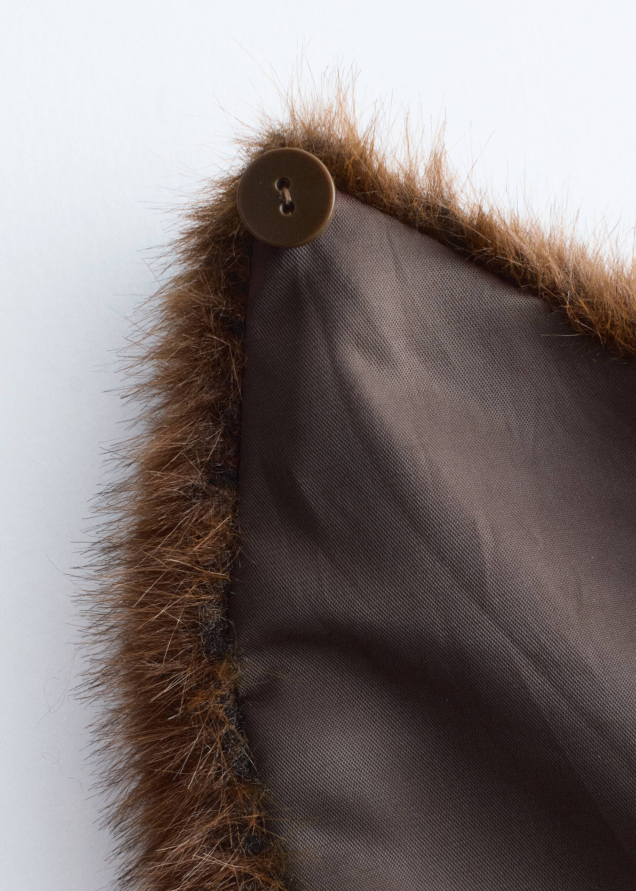 Se større billede: En Faux Fur Collar præsenteres, der viser sin lurvede brune faux fur kant langs den ene kant og en glat mørkebrun foring på bagsiden. En mørkebrun, to-huls knap bliver fastgjort i hjørnet af den pelskantede kant.