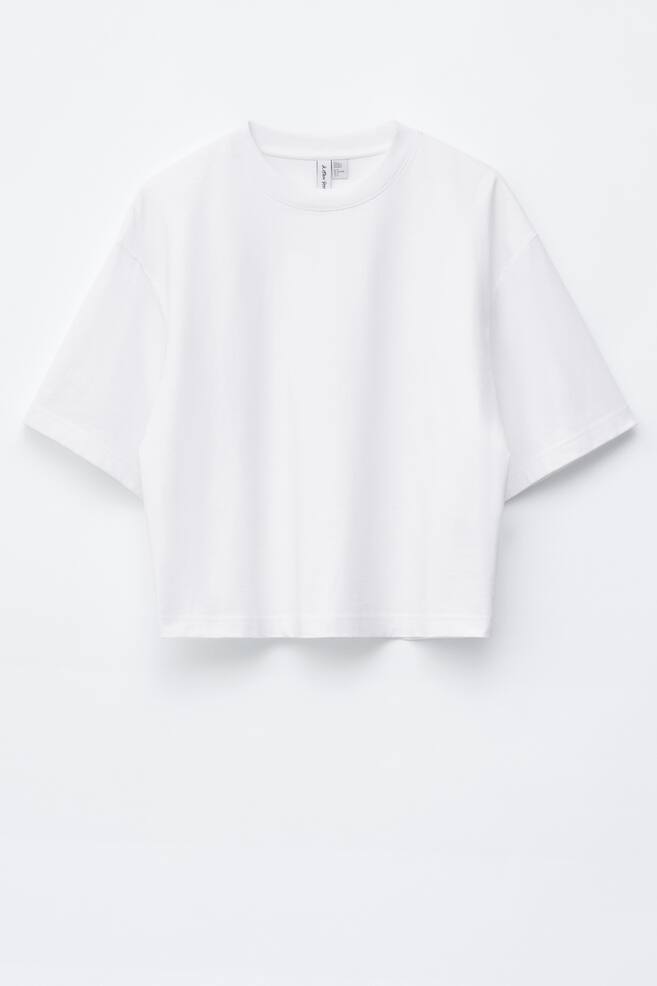 Ein weißes T-Shirt, gefertigt aus einem weichen Jersey-Stoff, wird von vorne gezeigt und verfügt über einen klassischen Rundhalsausschnitt und kurze, weite Ärmel. Es präsentiert eine entspannte, kastige Passform mit einem geraden, verkürzten Saum. - 1