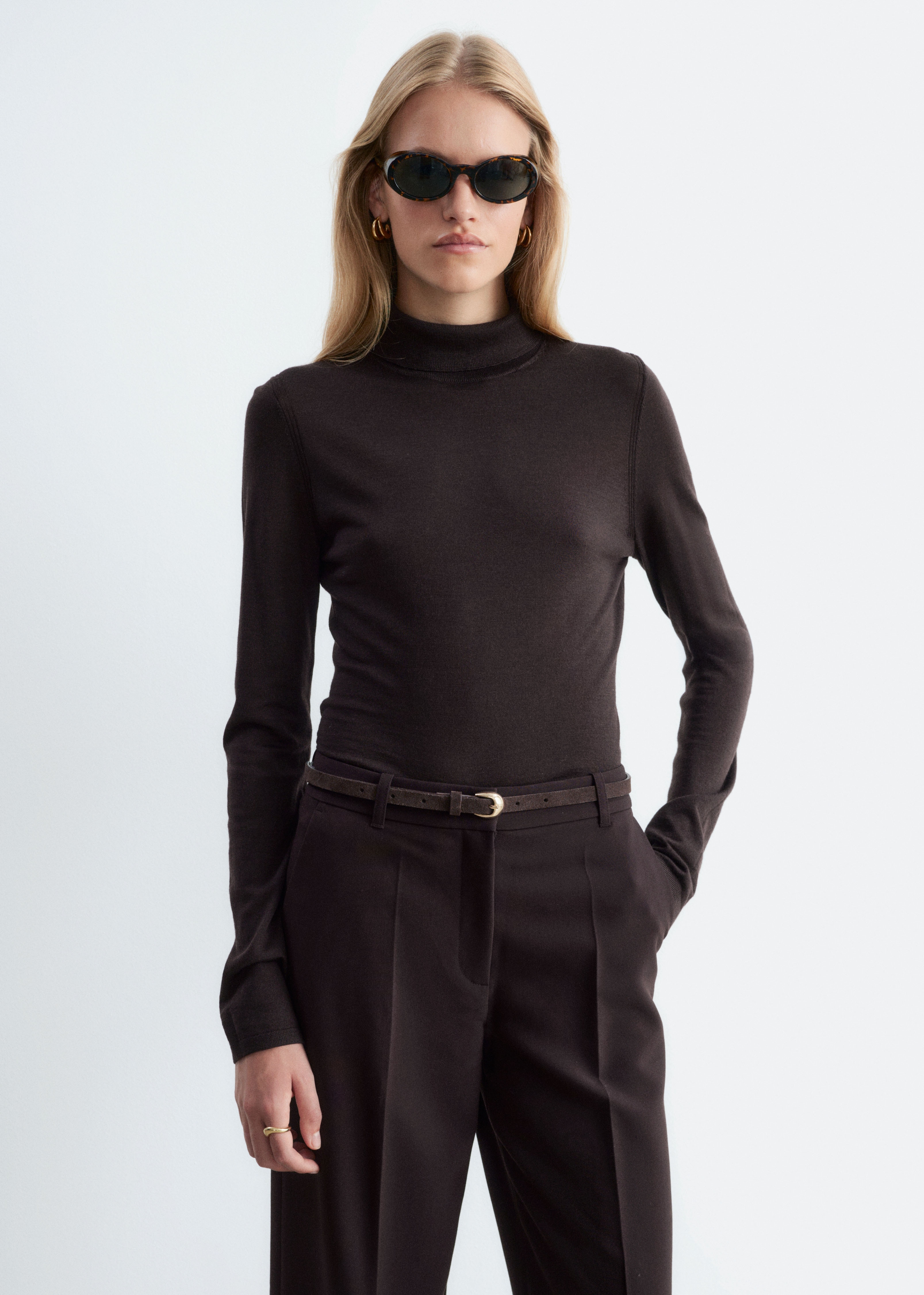 Ein dunkelbrauner, dünn gestrickter Rollkragenpullover wird flach und mit der Vorderseite nach oben gezeigt. Er verfügt über einen hohen, gerippten Kragen mit einem dezenten Rückenschlitz und langen, eng anliegenden Ärmeln mit schlichten Säumen.