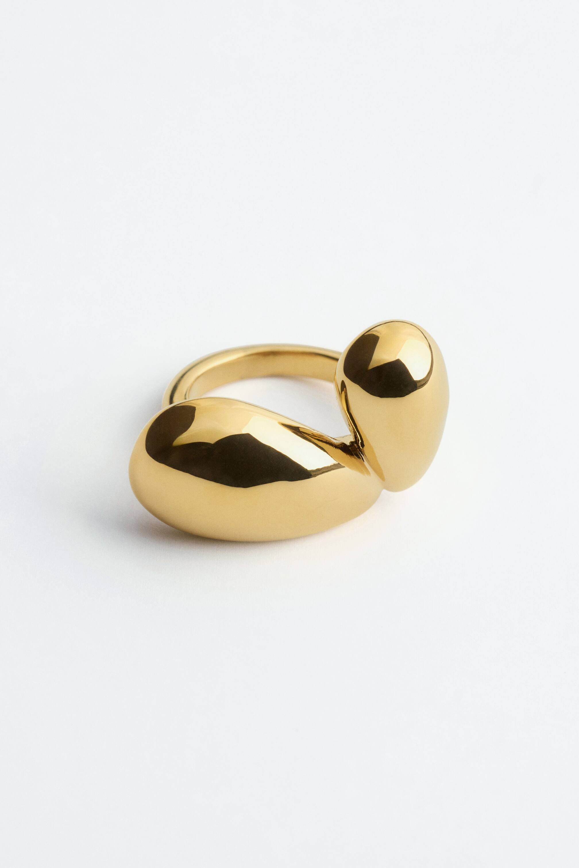 Agrandir l'image: Une bague en laiton doré poli est présentée sous un angle trois-quarts, mettant en valeur son design sculptural, avec un anneau lisse surmonté de deux formes fluides et bulbées. Sa surface hautement réfléchissante souligne les courbes organiques de la pièce.