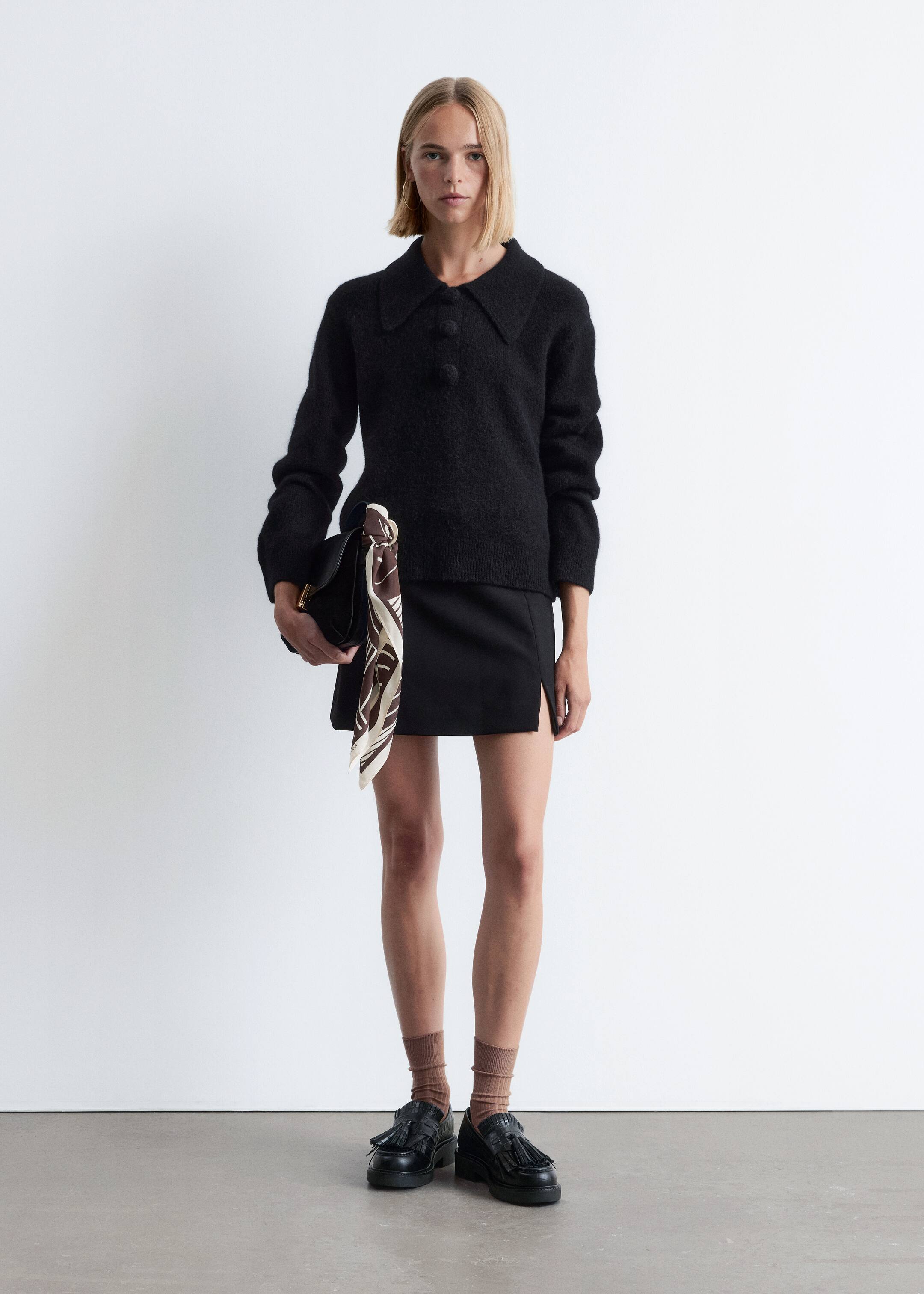 Visa större bild: En svart outfit presenteras, med en texturerad stickad topp i polostil med spridd krage och en treknappslå med sfäriska knappar, kombinerad med en svart minikjol som har en subtil lårslits. Ensemblen kompletteras med svarta chunky loafers med dekorativ frans och tofsar, bärs med ribbade ljusbruna strumpor och en svart handväska prydd med en mönstrad scarf.