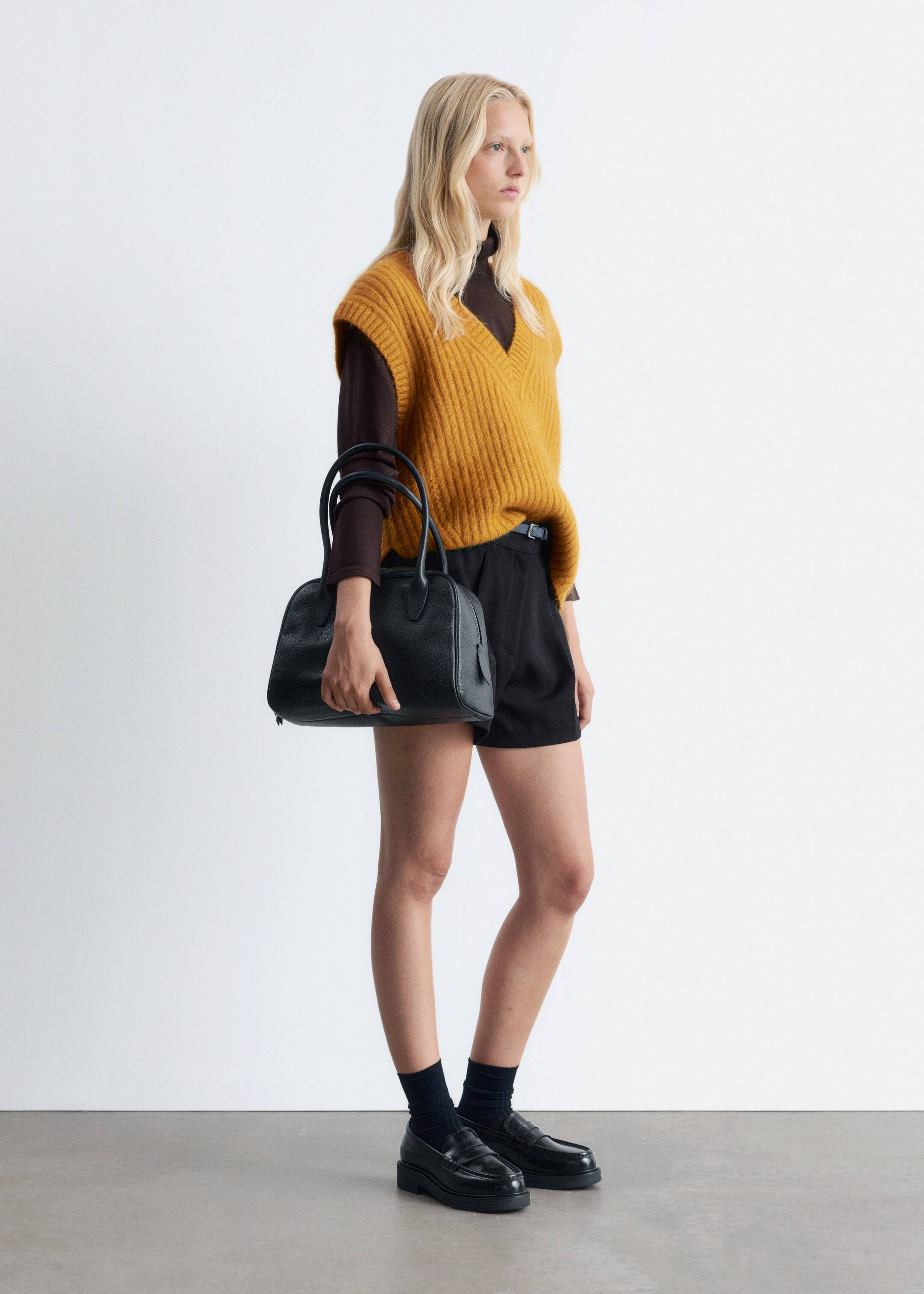 View larger image: A yellow V-neck vest with a rib-knit finish is being worn by the model, layered over a dark long-sleeved top. The vest features a loose fit.