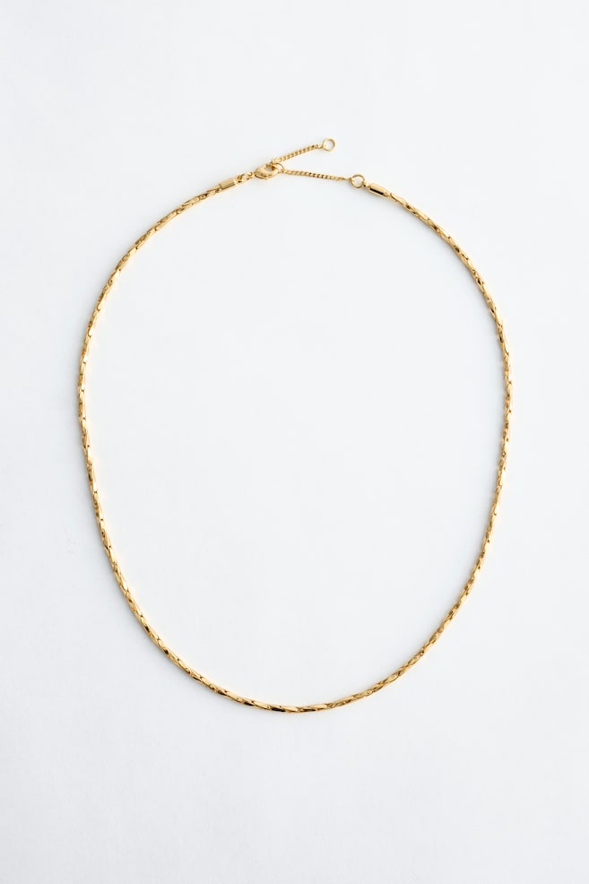 A polished, gold-toned chain necklace is displayed at its full length, forming an open circle. It features a flexible chain of short, flat, interconnected links and showcases a lobster clasp with an extension chain at the top. - 1