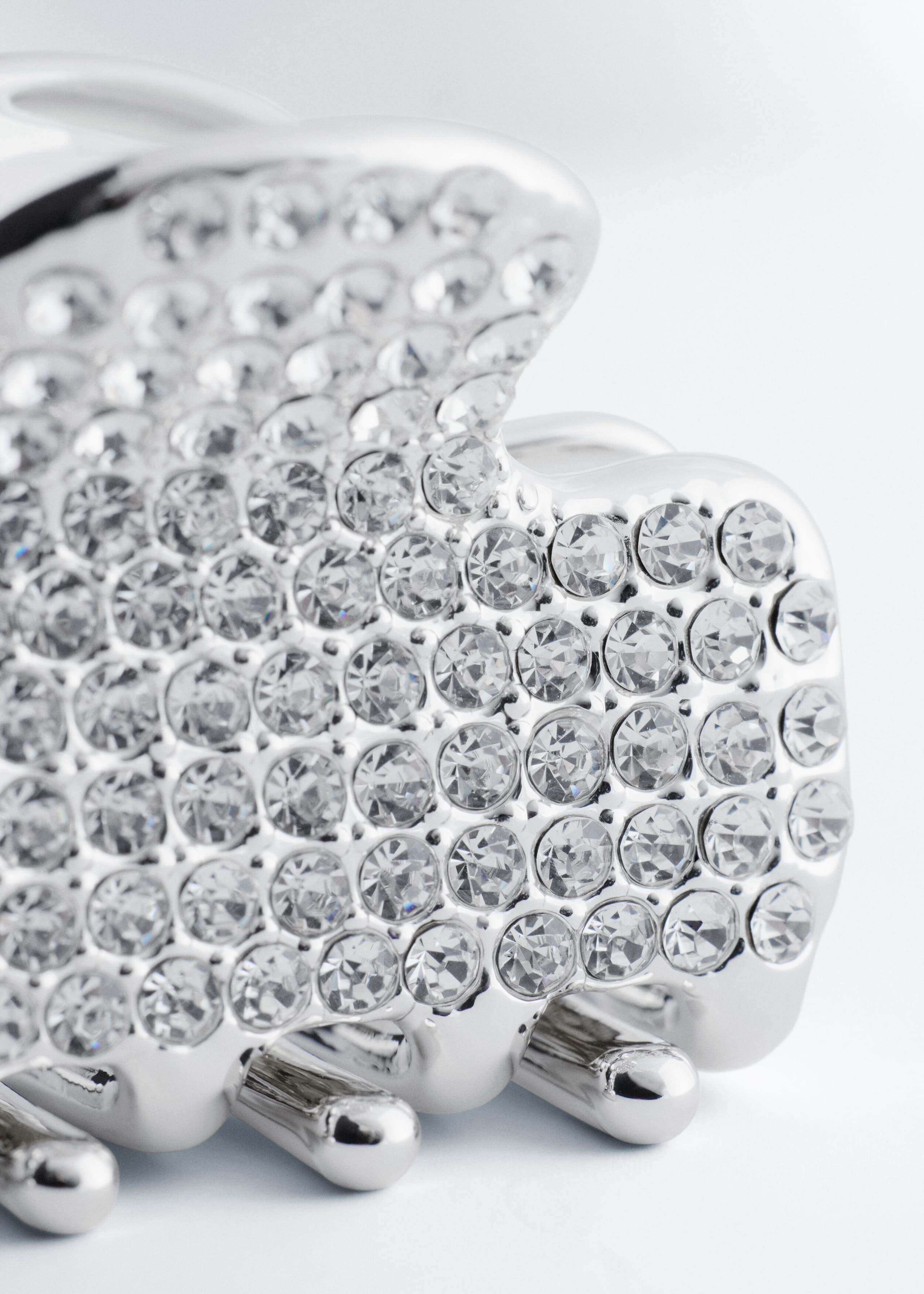 A silver-toned hair claw clip features a curved outer body densely embellished with round, faceted clear rhinestones. Smooth, polished metallic prongs extend downward from the base of the clip.
