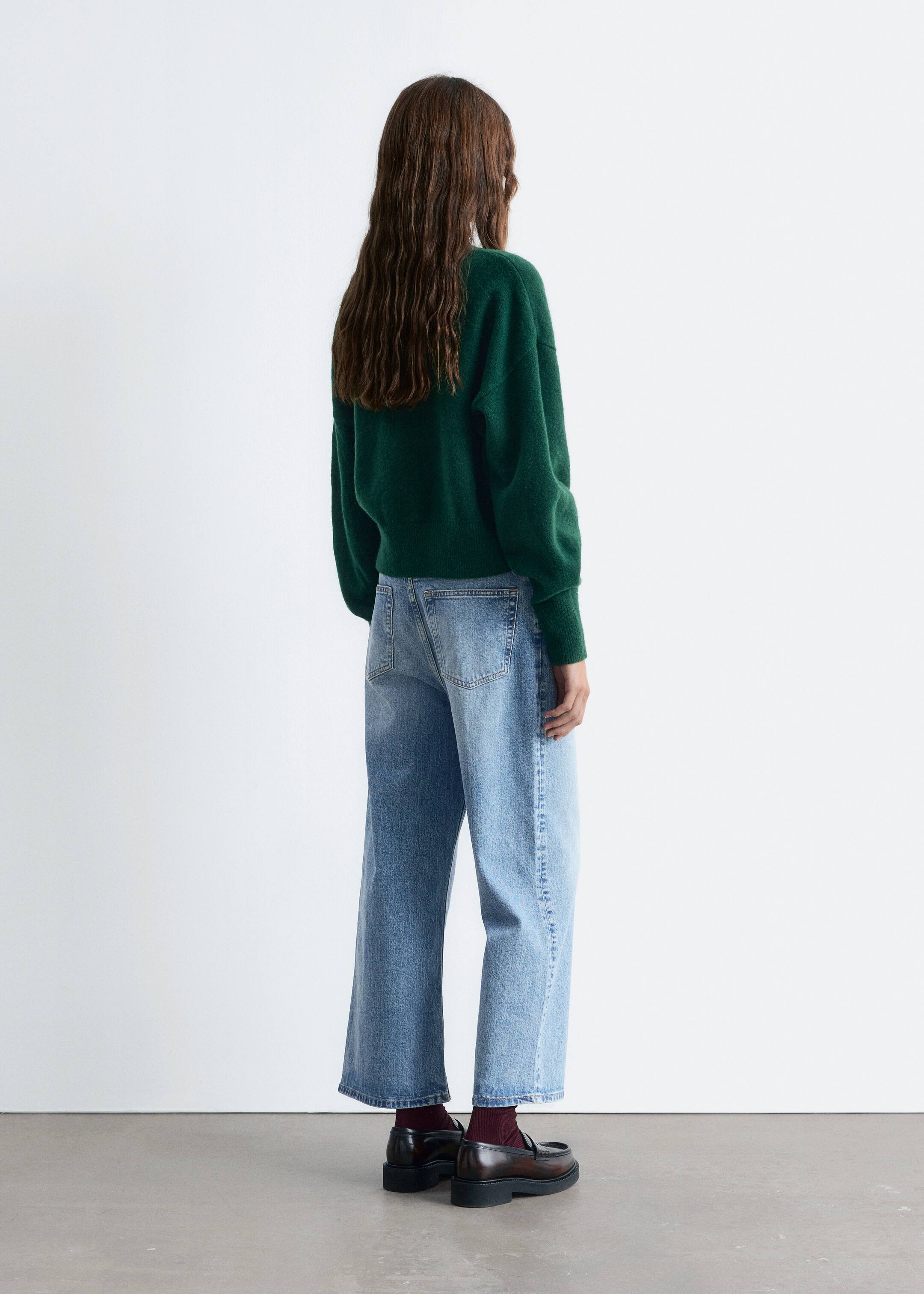 Visa större bild: En mörkgrön, mjuktröja med ribbade muddar och fåll bärs, sedd bakifrån, ihop med ljusblå, vida jeans med en blekt tvätt. Mörkbruna loafers med tjock sula kompletterar looken och avslöjar vinröda strumpor.