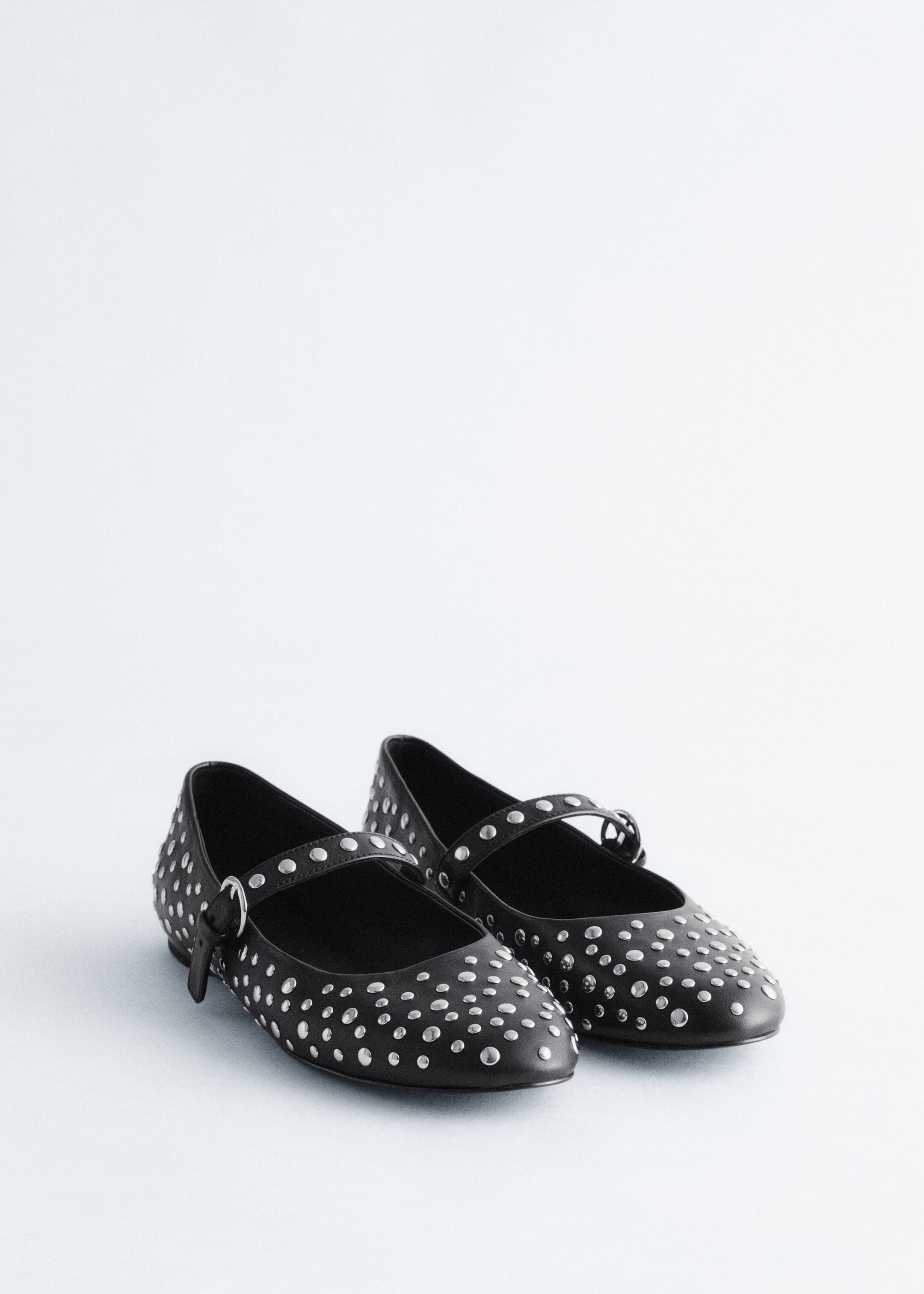 View larger image: A pair of black leather Mary Jane ballet flats is sitting, being covered in allover silver-toned metal studs. Each shoe is featuring a strap across the instep, which is being secured by a silver-toned buckle.