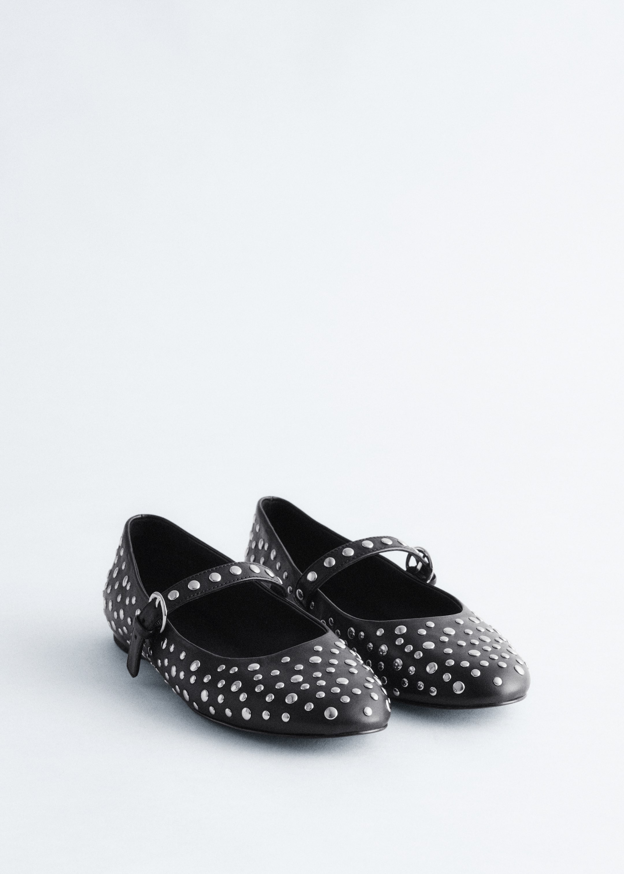 View larger image: A pair of black leather Mary Jane ballet flats is sitting, being covered in allover silver-toned metal studs. Each shoe is featuring a strap across the instep, which is being secured by a silver-toned buckle.