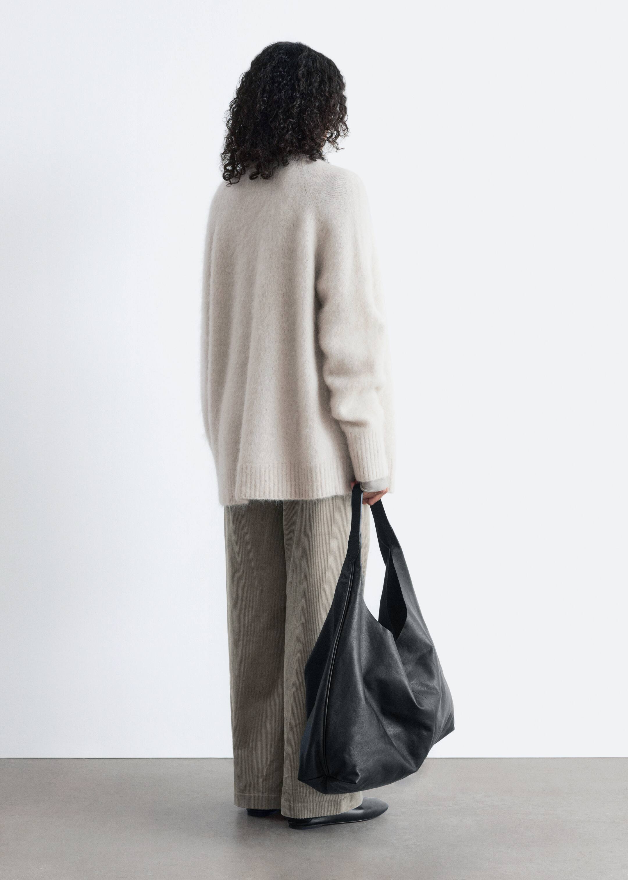 View larger image: A large, black unstructured bag is being carried by its wide strap, facing back-right. Its soft material is displaying a matte finish and a slouchy silhouette.