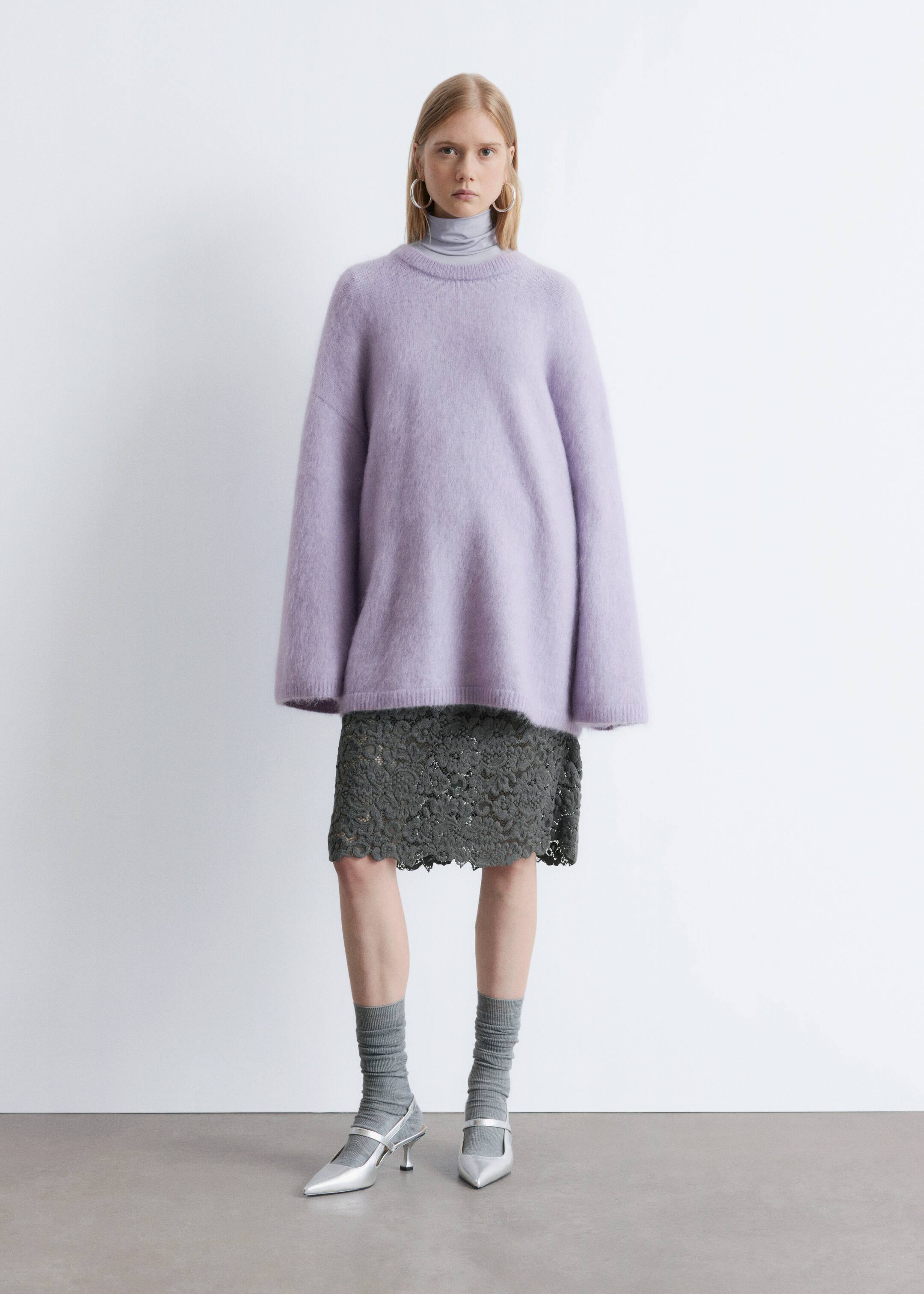 Agrandir l'image: Un pull lilas à col rond est présenté de face, avec une texture duveteuse et une coupe ample et décontractée avec de longues manches larges. Il est superposé à un col roulé gris et une jupe en dentelle verte.